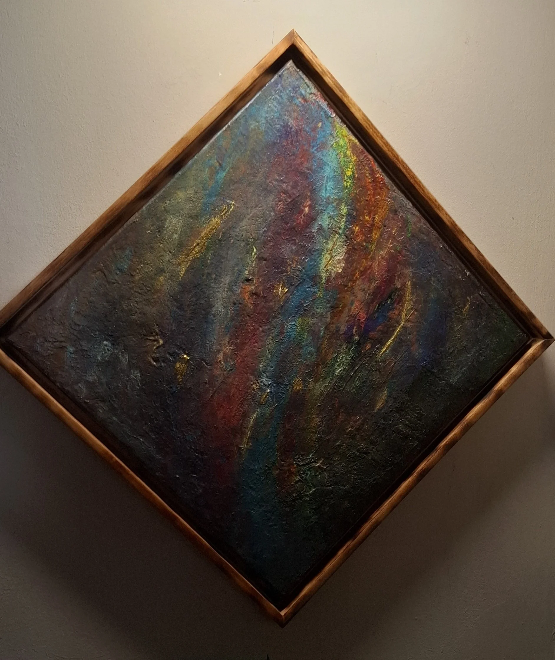 Abstraktes, farbenfrohes Gemälde in einer dekorativen Holzrahmung, aufgehängt an einer weißen Wand.