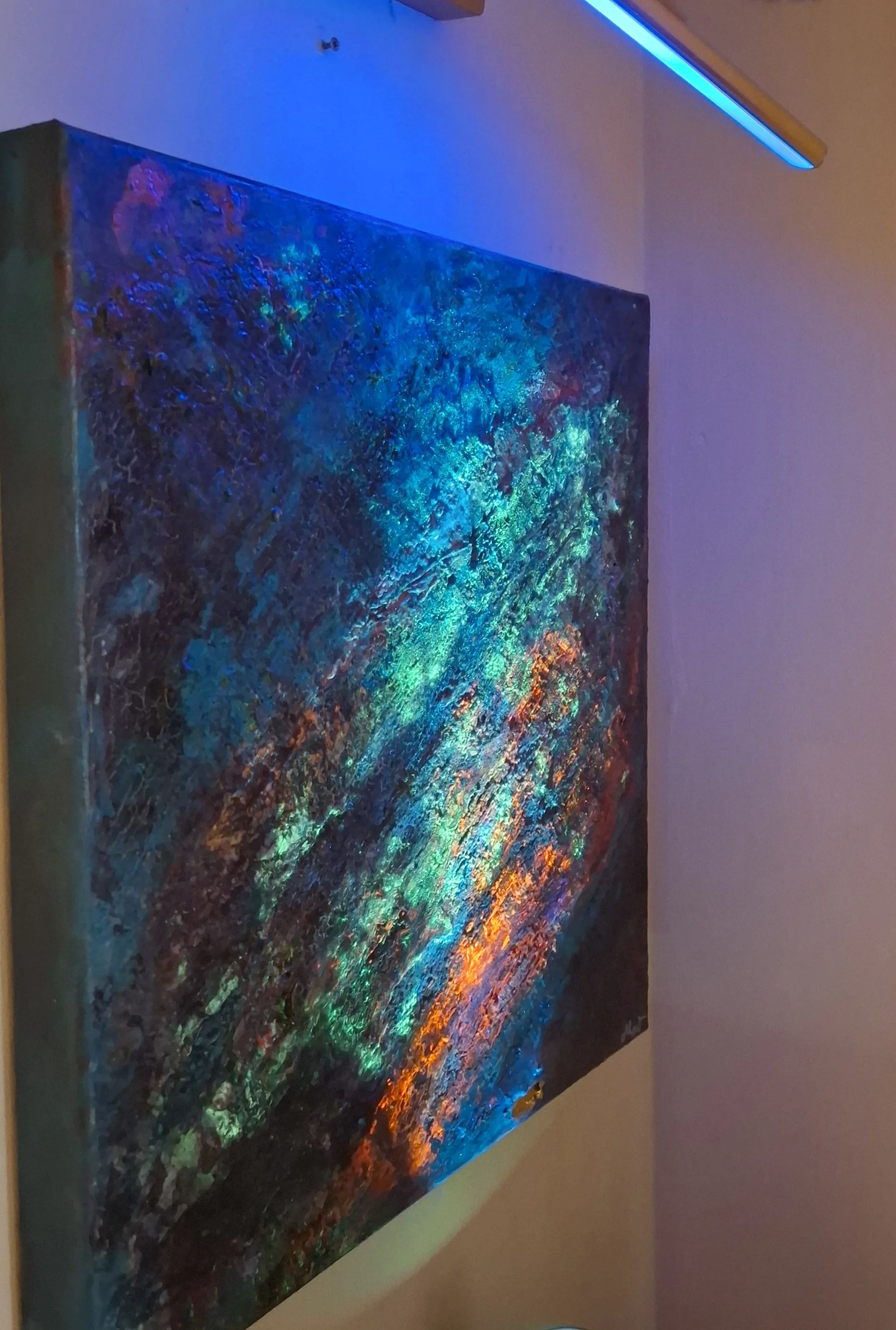 A colorful abstract painting with vibrant colors and texture, illuminated with a blue light.