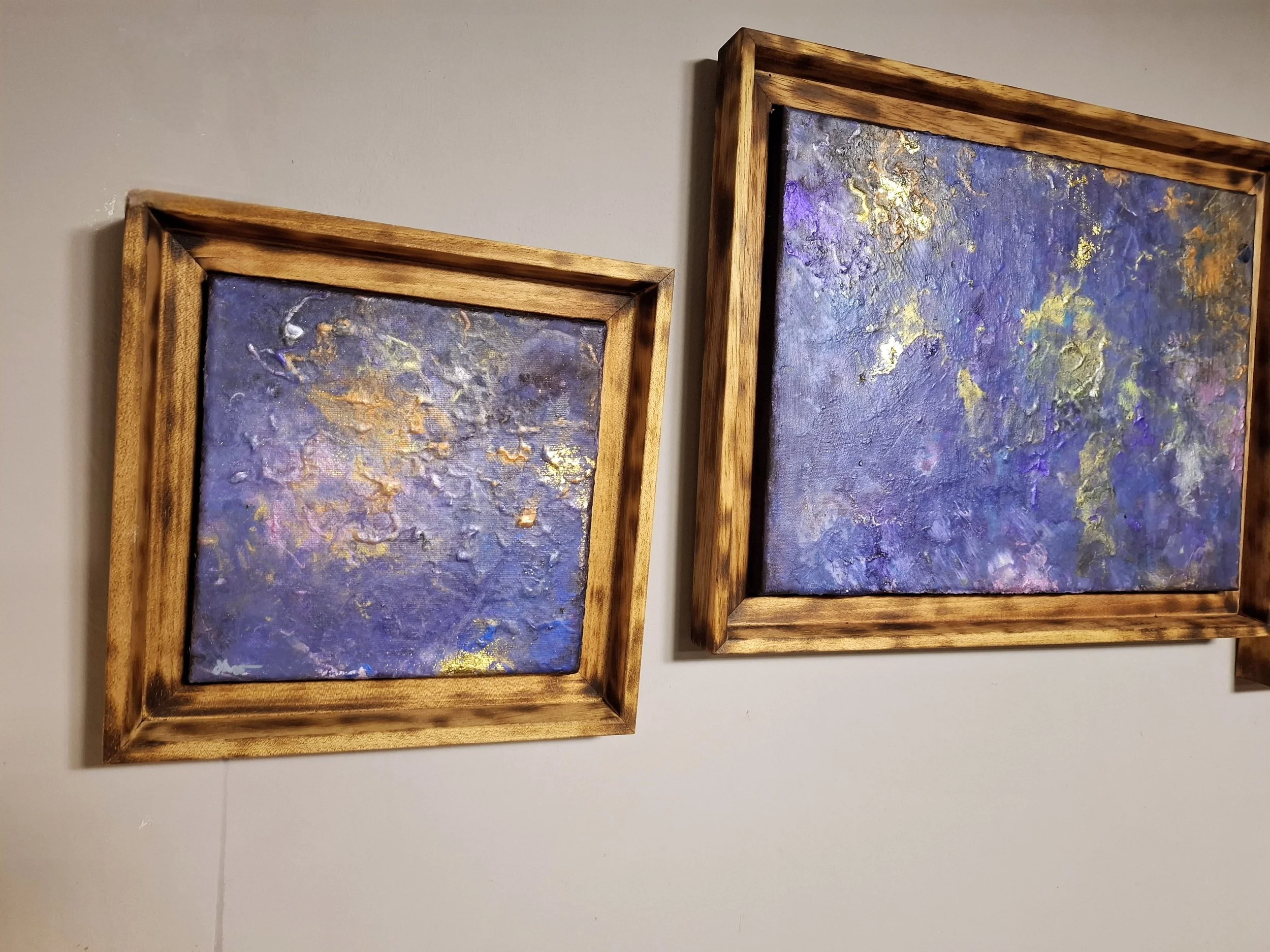 Zwei abstrakte Gemälde mit dominanten Lilatönen in hölzernen Rahmen, nebeneinander an einer weißen Wand.