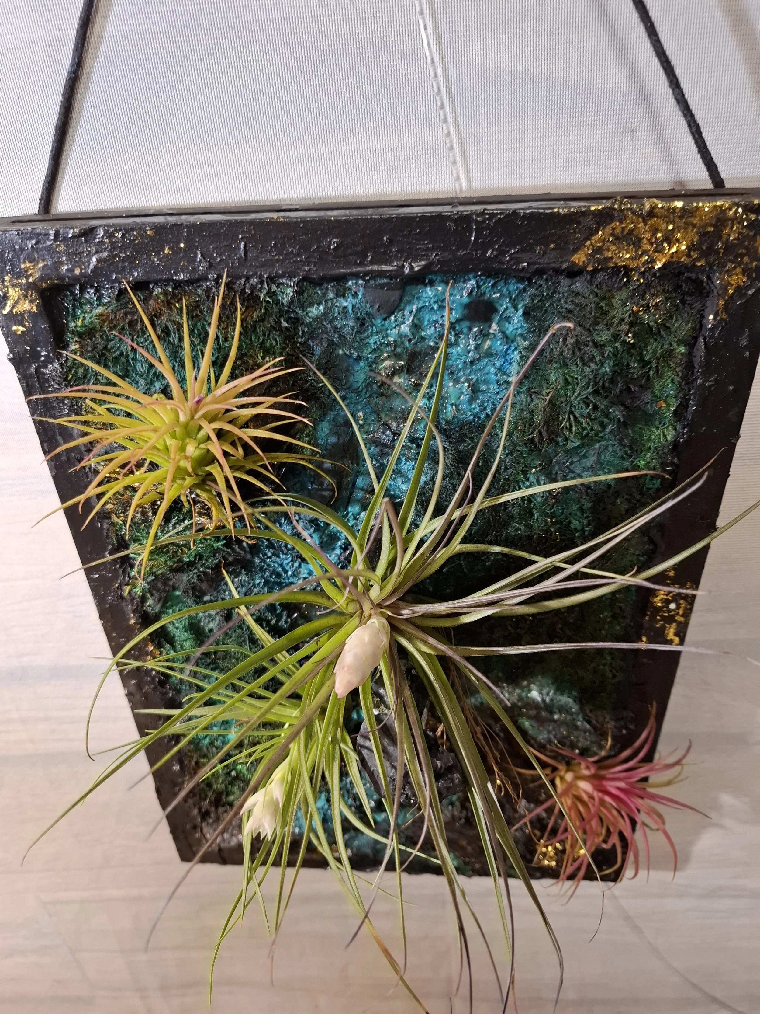 Kunstpflanzen in einer dekorativen Wandinstallation mit bunten mineralischen Elementen.