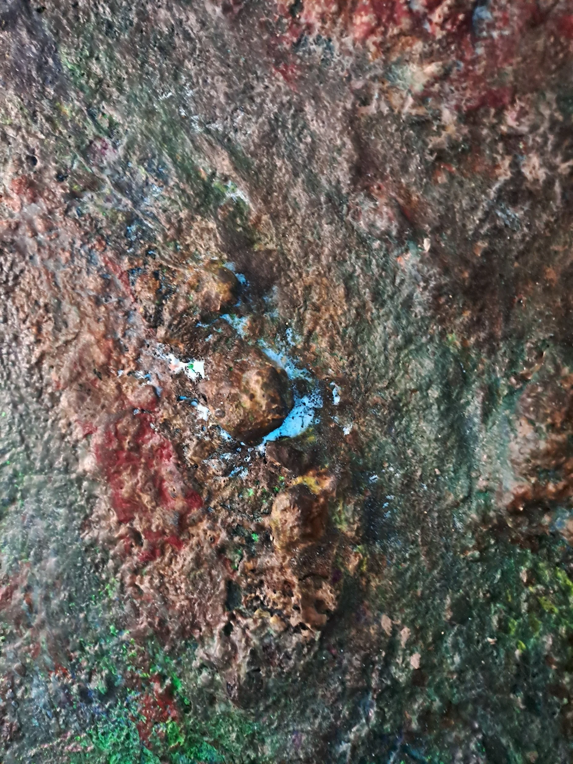 Eine Nahaufnahme einer rauen und mit bunten Flecken bedeckten Oberfläche, die wie eine skulpturale Textur wirkt.