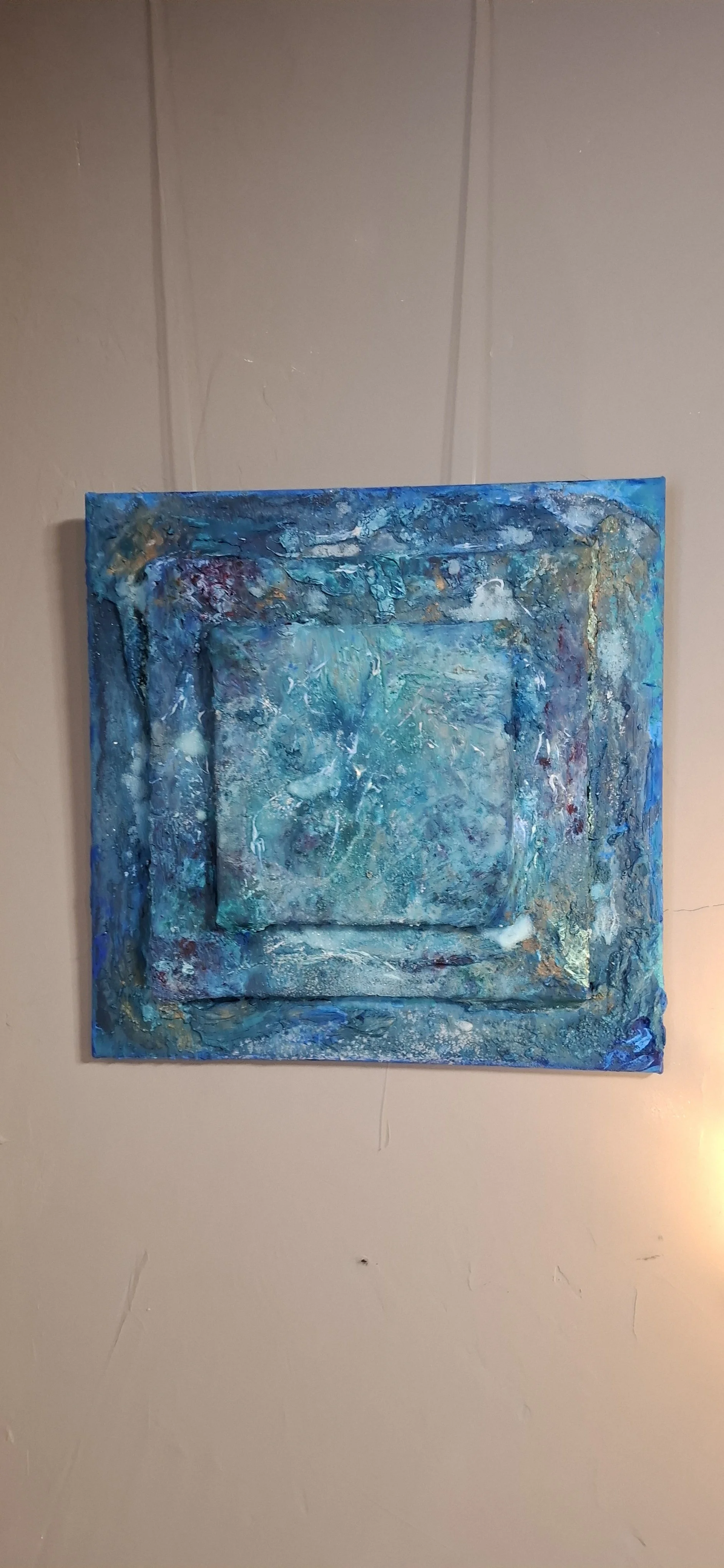 Abstraktes Gemälde in Blau- und Türkistönen, die auf einer beige Wand hängen.