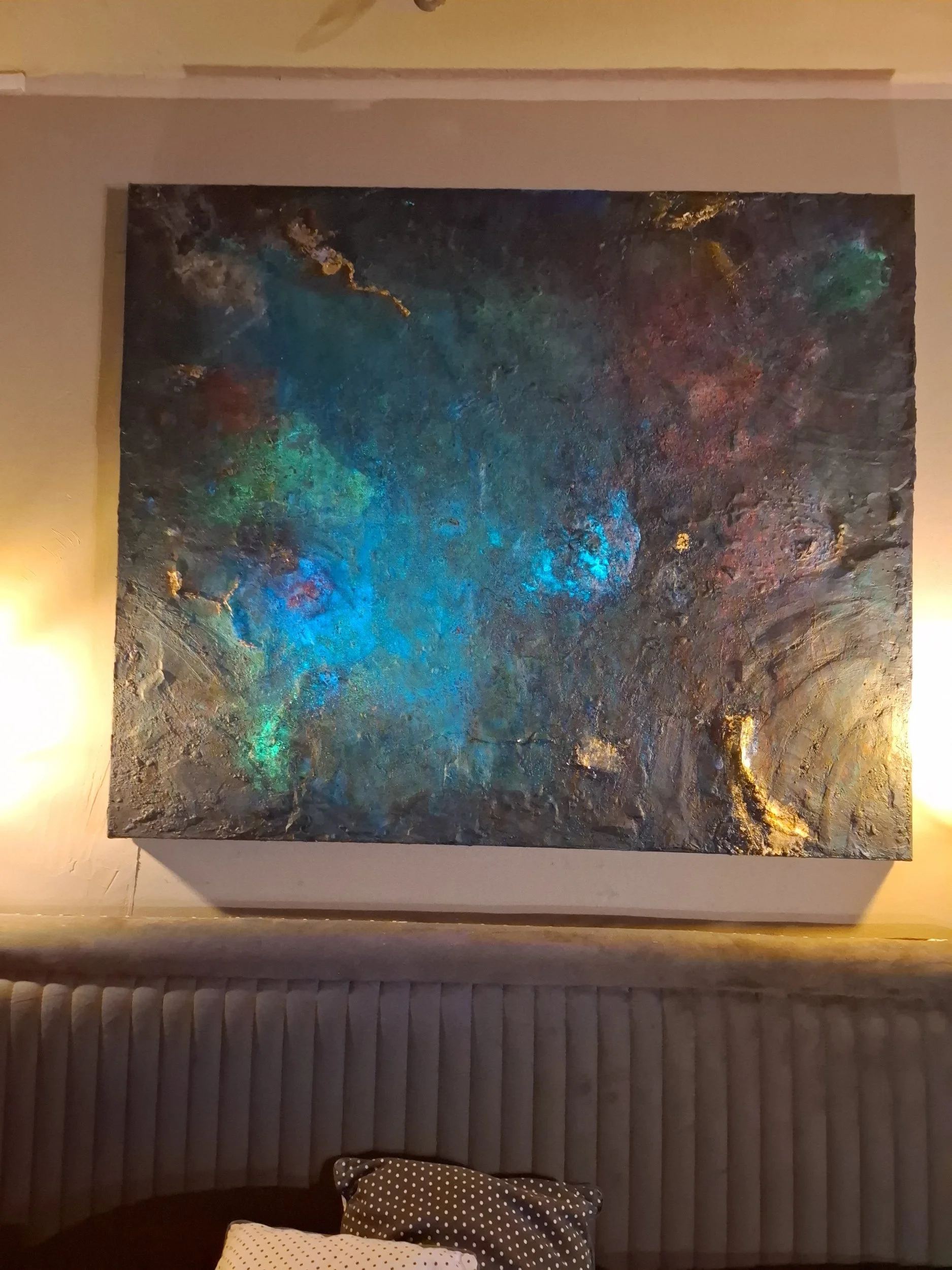 Abstraktes Gemälde mit dunklen, leuchtenden und goldfarbenen Akzenten an einer Wand über einem polierten Boden mit Holzfliesen.
