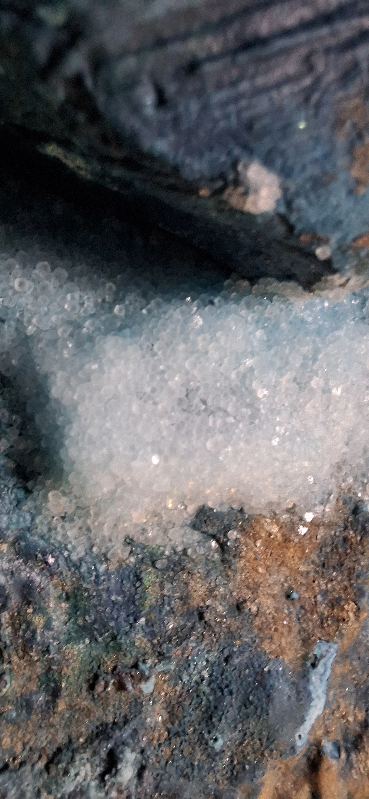 Sand, Steine und eine schwarze Holzstange auf dem Boden in einer Höhle oder einem natürlichen Raum.
