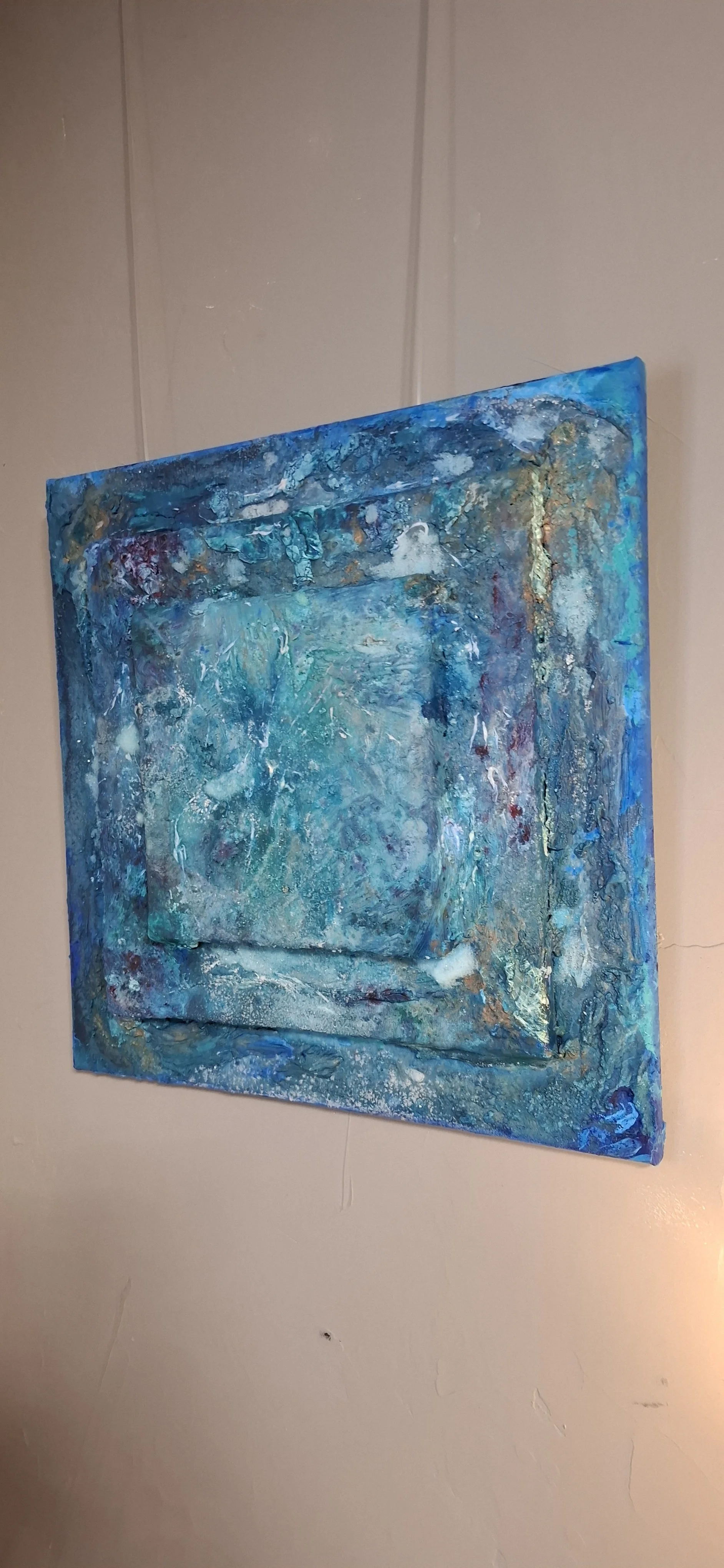 Abstraktes, aquarellartiges Gemälde in Blau- und Türkistönen an einer Wand. Das Kunstwerk ist mehrschichtig und texturiert.