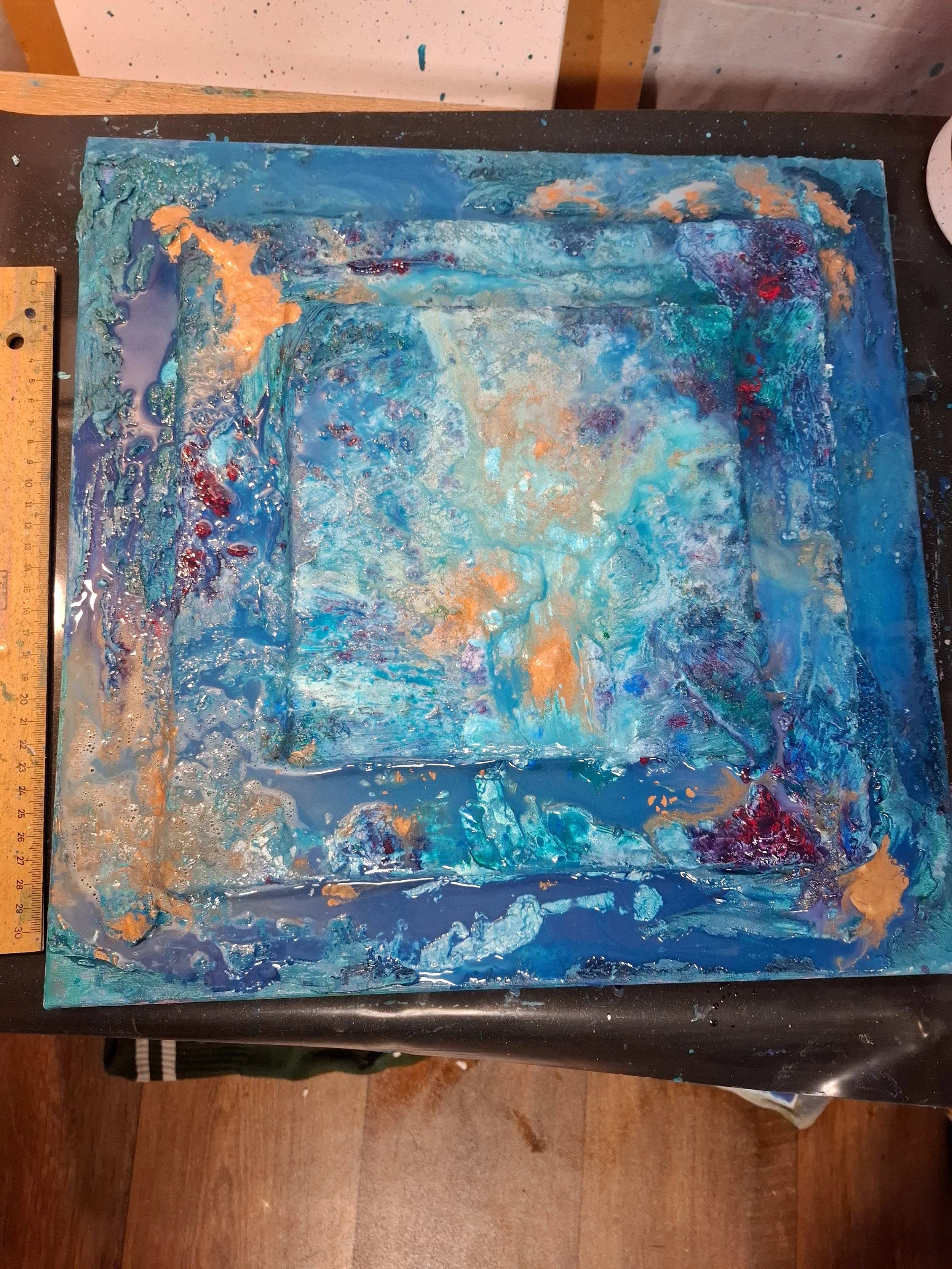 Abstraktes Gemälde in Blau und Türkis mit orangefarbenen Akzenten, auf einem Tisch liegend.