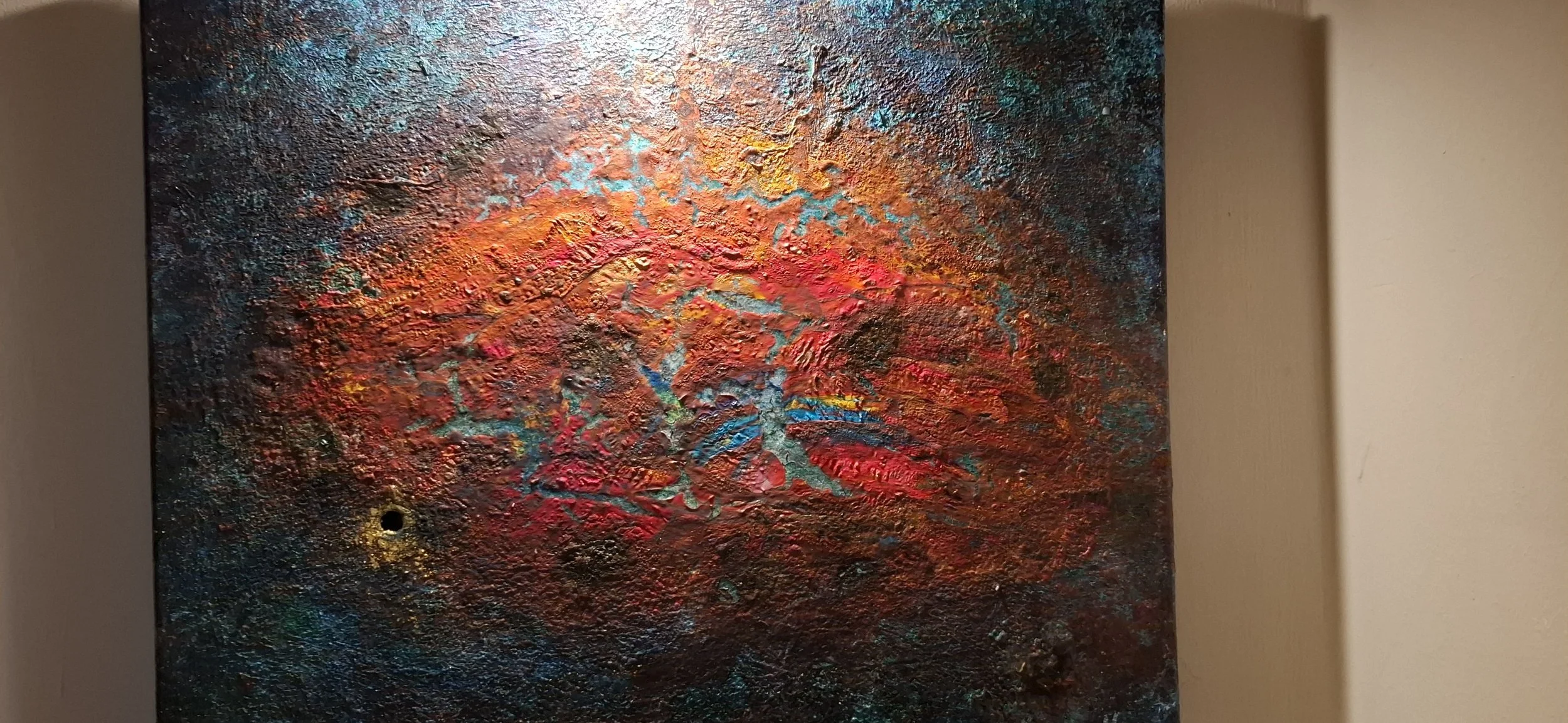 Abstraktes, farbenfrohes Gemälde mit texturierter Oberfläche in Rottönen, Blau und Gelb, an einer Wand aufgehängt.