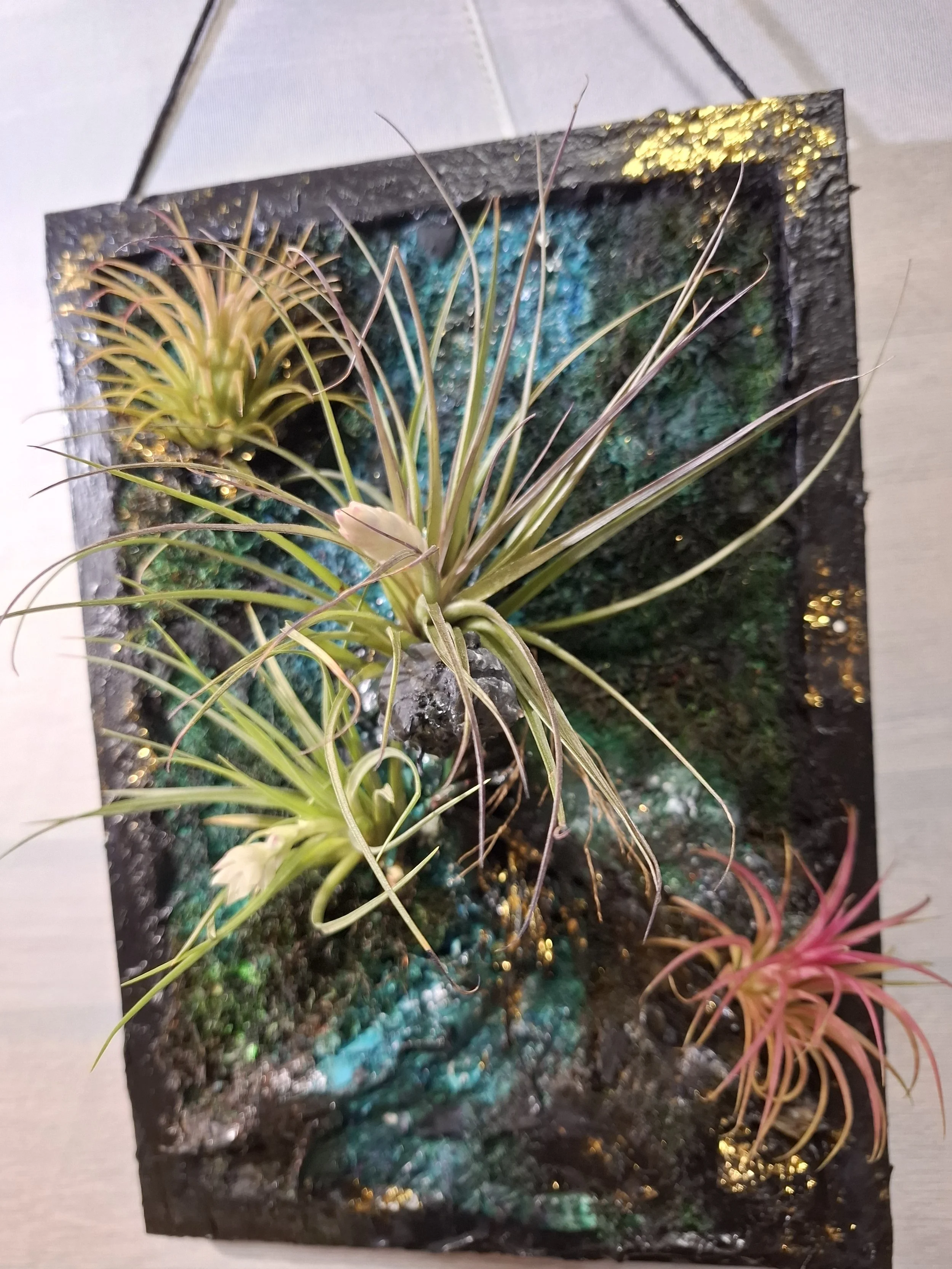 Kunstpflanzen in einem rechteckigen Rahmen mit bunten, langen Blättern, auf einer Holzoberfläche platzieren.