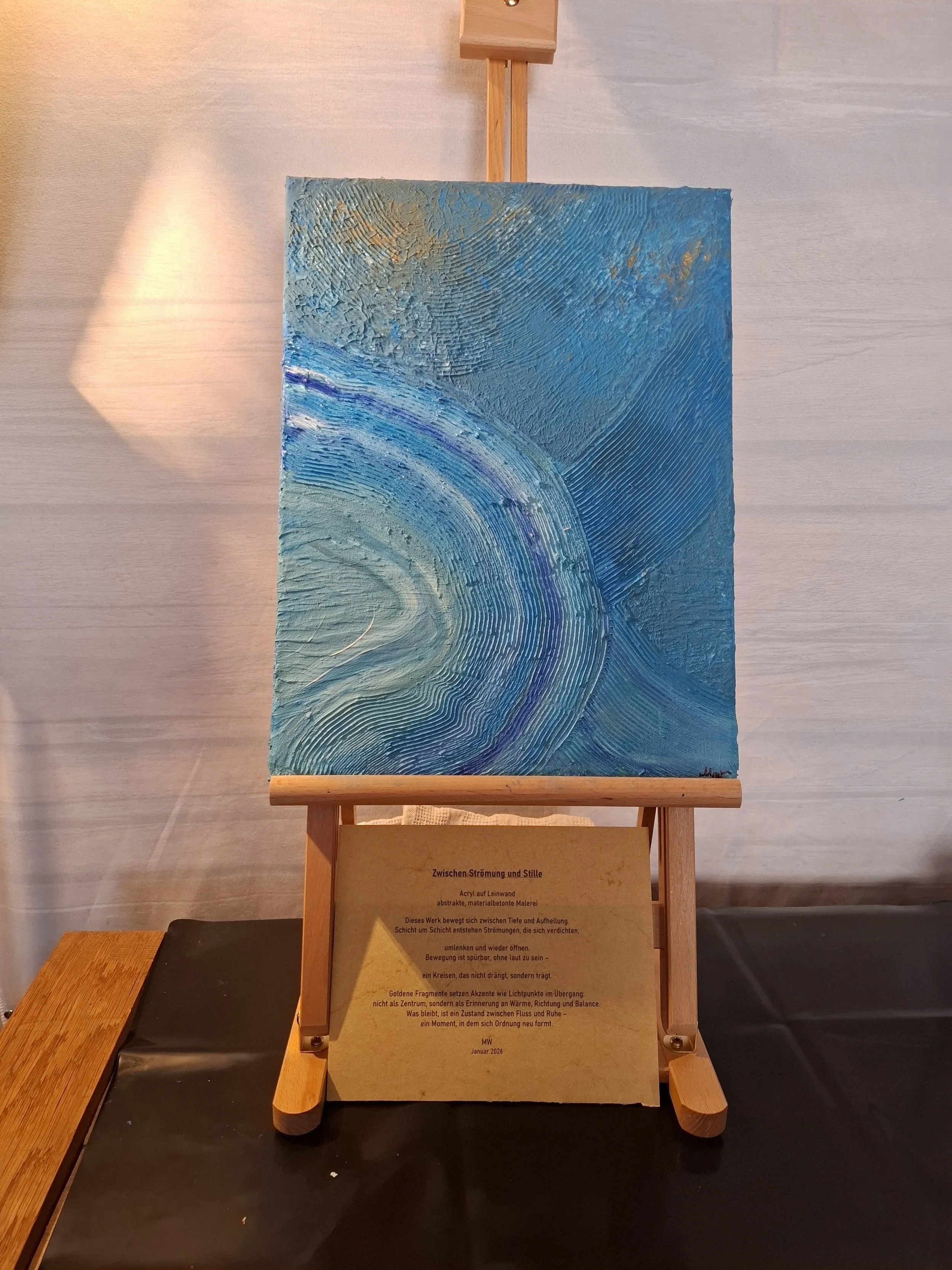 Ein abstrakes Gemälde in Blau- und Türkistönen auf einem Holzständer, mit einer Beschreibung auf einem Schild darunter.