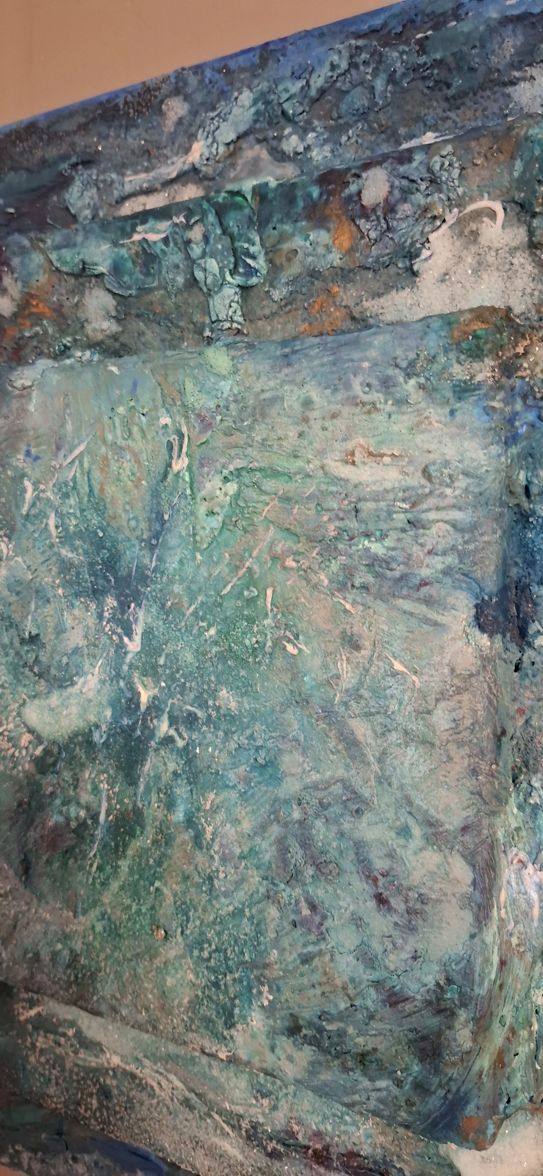 Nahaufnahme einer abstrakten, strukturierte Kunstskulptur mit blauen, grünen, weißen und braunen Farbtönen aus dicker, pastöser Farbe. Das Kunstwerk hat eine raue, unregelmäßige Oberfläche.