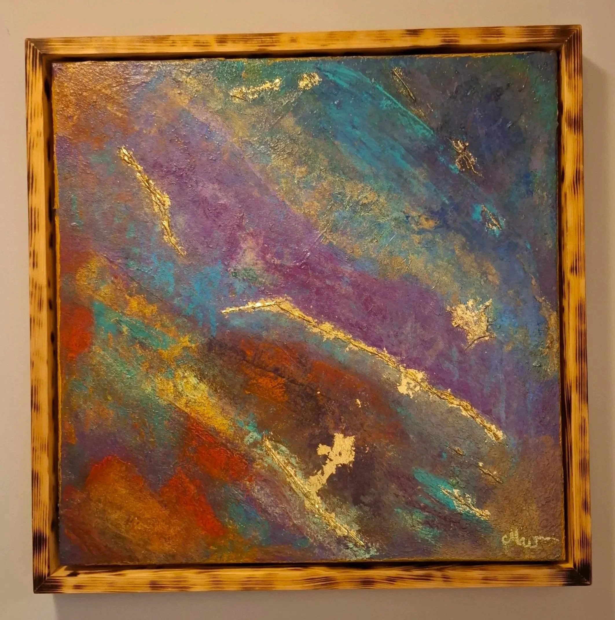 Ein abstrapptes Gemälde mit bunten, gemischten Farben und Goldakzenten, in einem Holzrahmen.