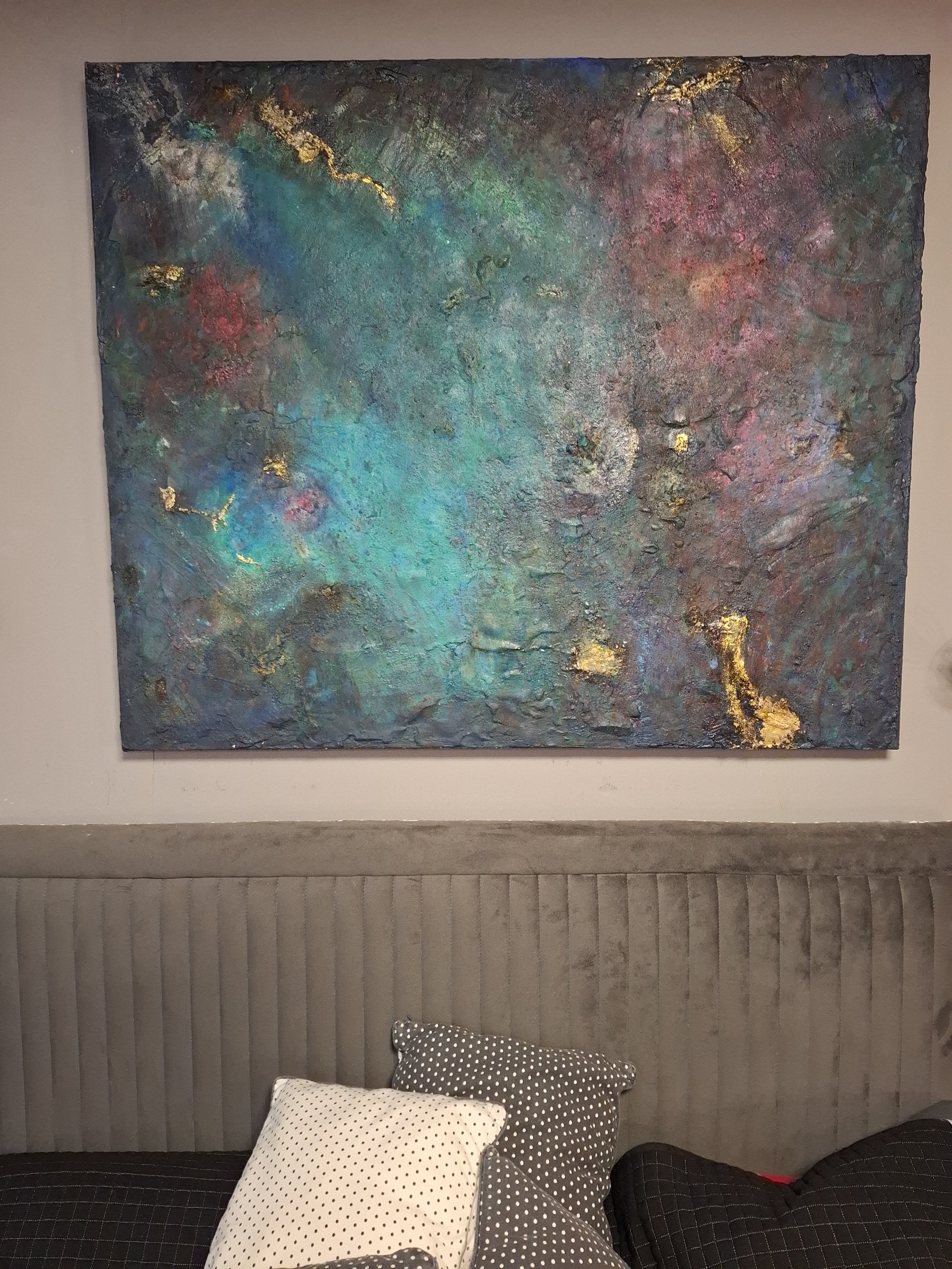 Ein abstraktes Gemälde an einer grauen Wand über einem Brauchesofa mit schwarzen, weißen und gemusterten Kissen.