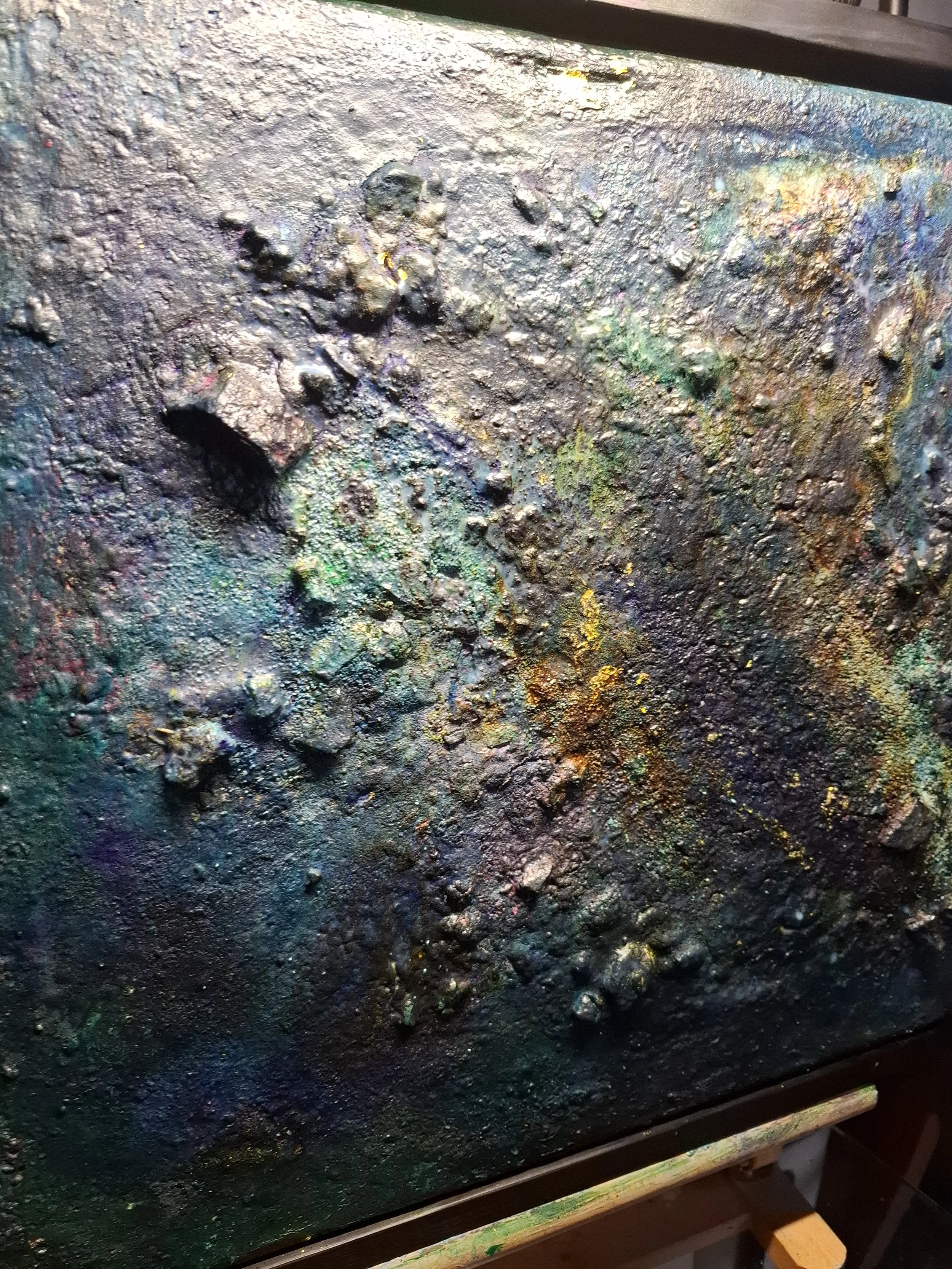 Eine Oberfläche, die mit dunkler, grobkörniger Farbe bedeckt ist, mit kleinen, leuchtenden Farbspritzern in verschiedenen Farben, die an einen abstrakten, nassen Malerei-Lack erinnert.