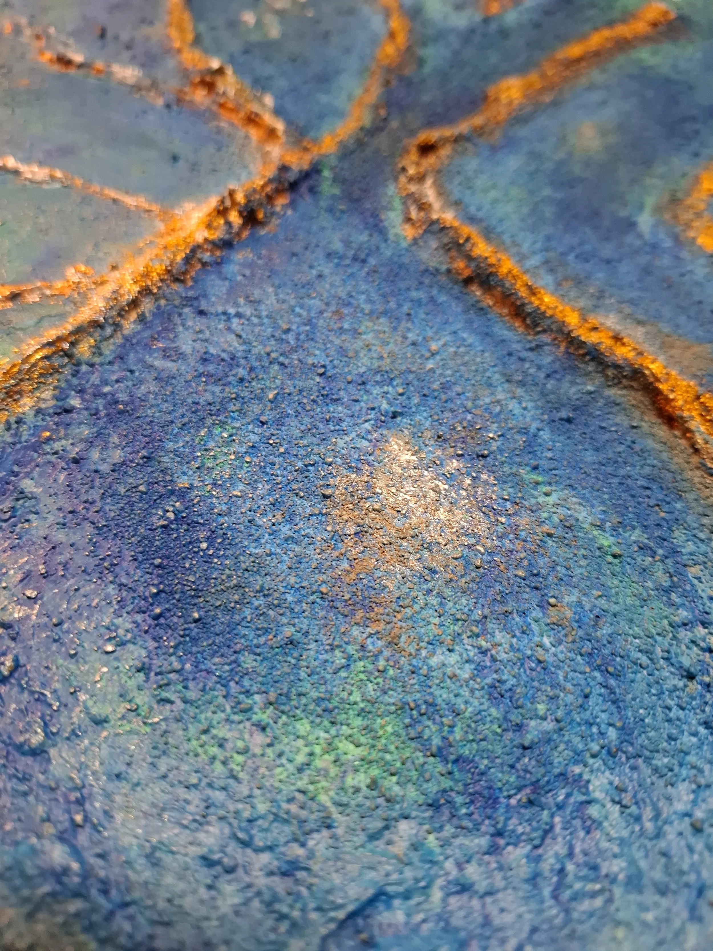 Nahaufnahme von einer bunten, sandartigen Oberfläche mit blauen, grünen und orangefarbenen Pigmenten und Texturen.