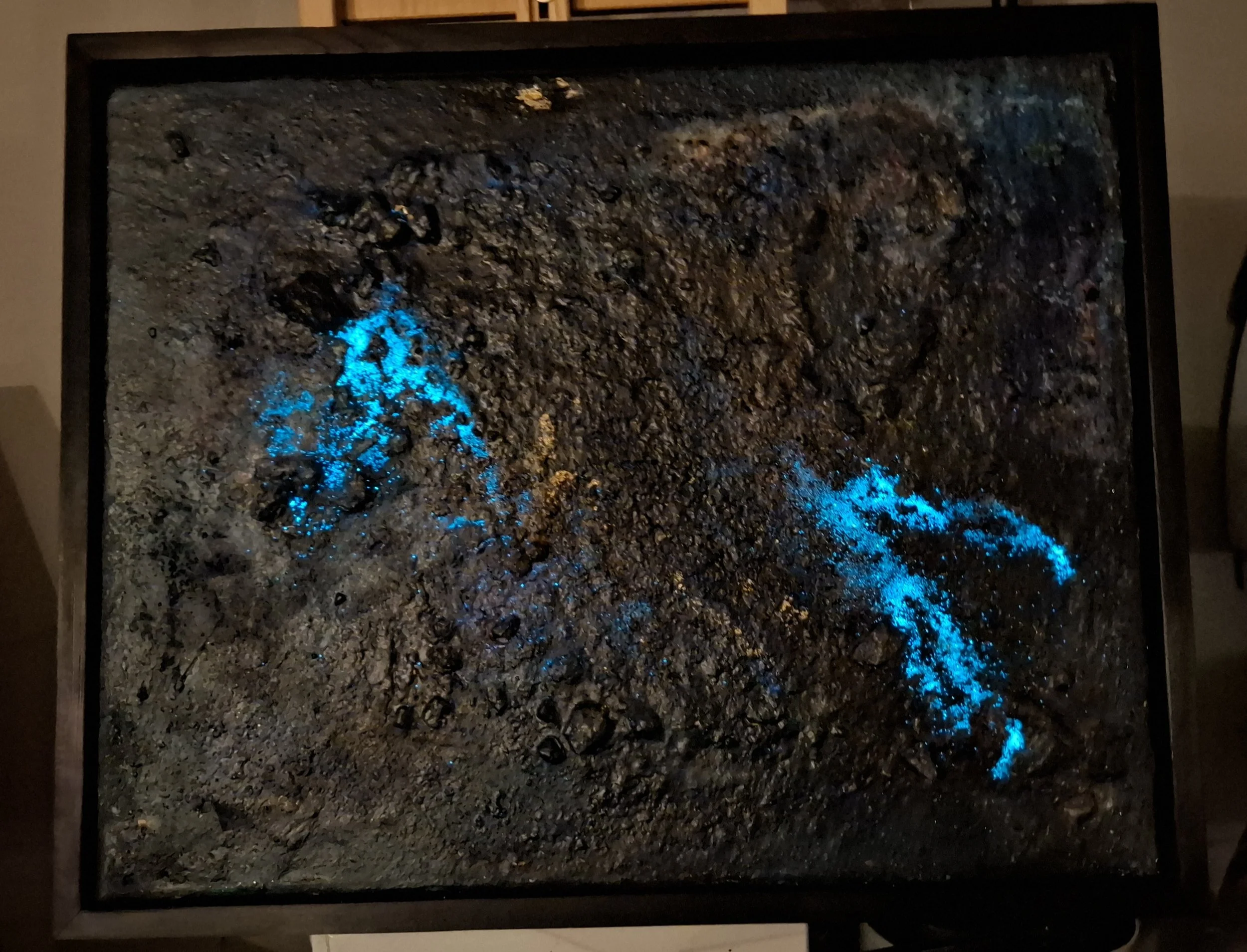 Ein Bild von einer Erdfläche mit glühenden blauen Stellen, vermutlich heiße Lava oder Magma, eingeschlossen in einem Rahmen, vermutlich ein Gemälde oder eine Nachbildung.