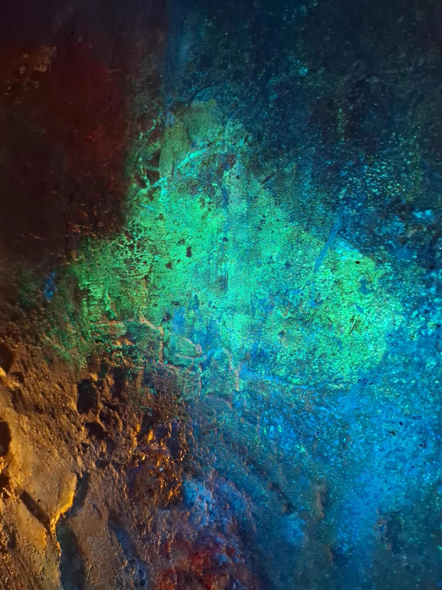 Ein bunter, leuchtender See mit schimmernden, irisierenden Farben wie Blau, Grün und Gold. Es scheint, als läge der See in einer Höhle oder in einem abgelegenen Gebiet mit mineralreichen Böden.