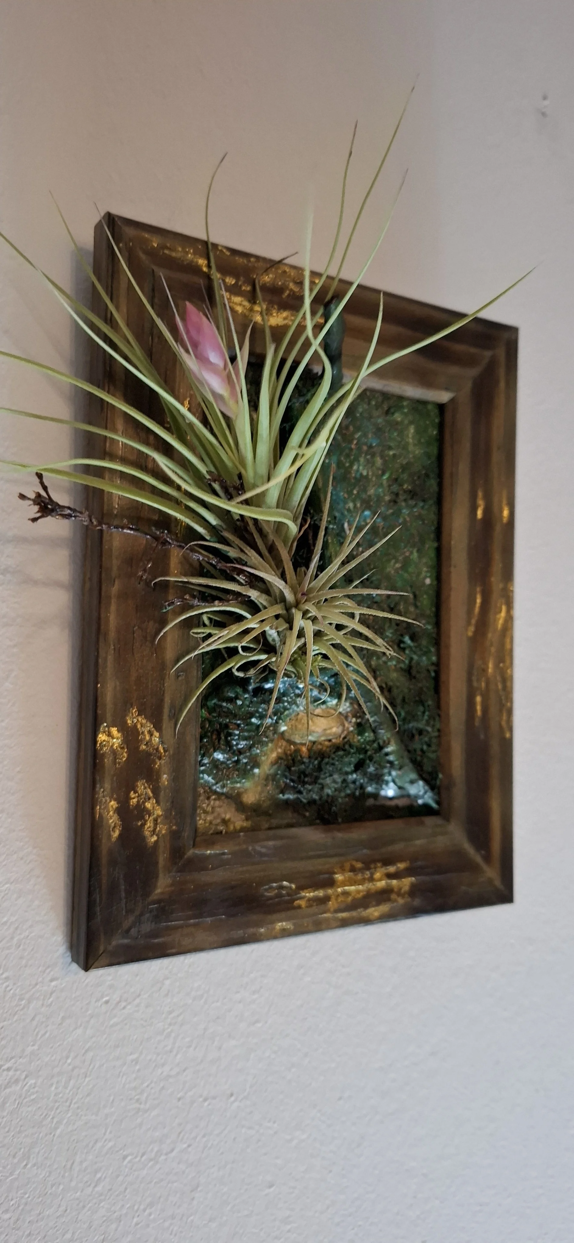 Kunstblumen in einer Holzrahmen mit goldfarbenen Details, Montage an einer weißen Wand.