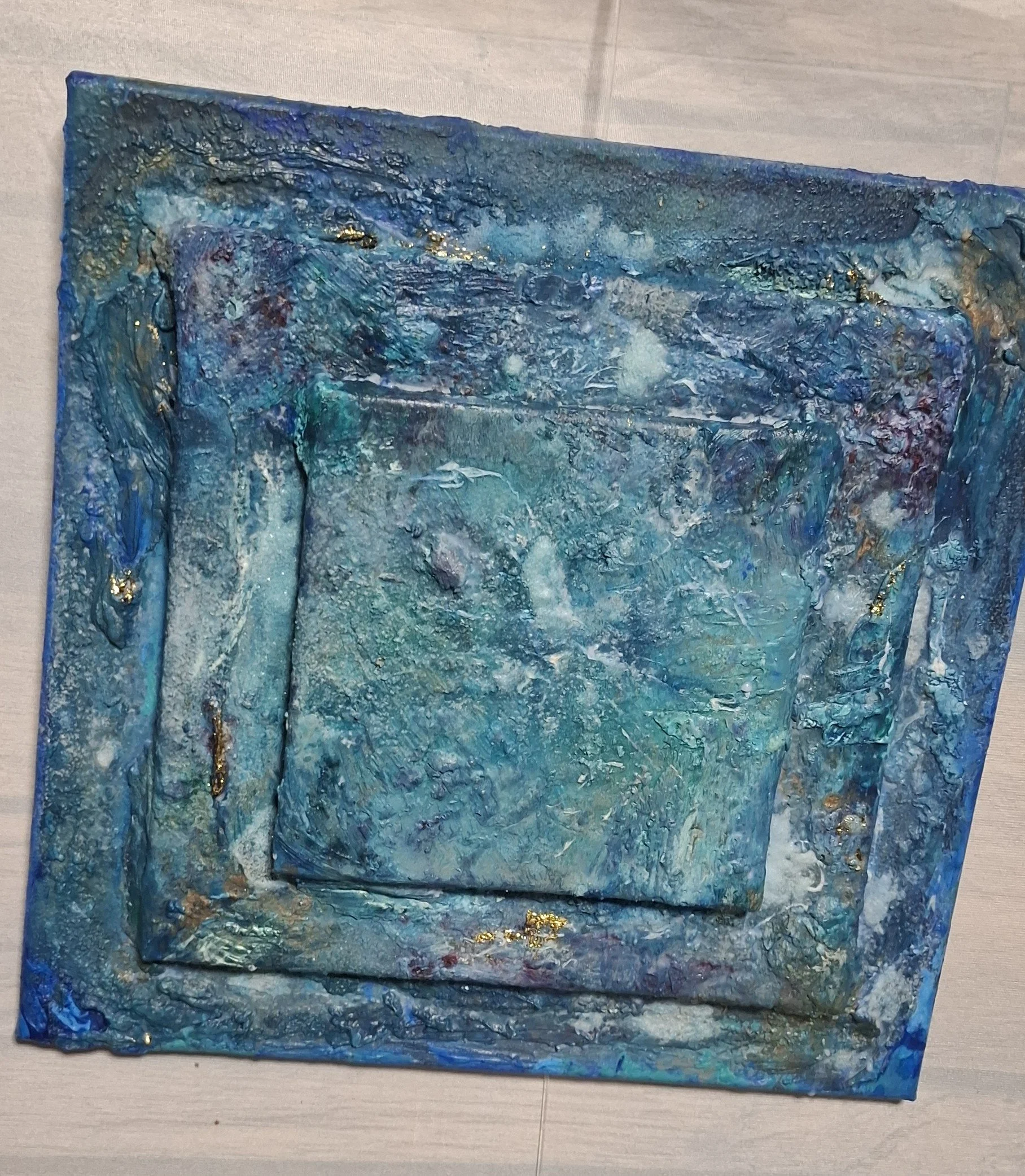 Ein abstraktes Wandbild mit überwiegend blauen und türkisen Farben, goldenen Akzenten und einer strukturierten Oberfläche.