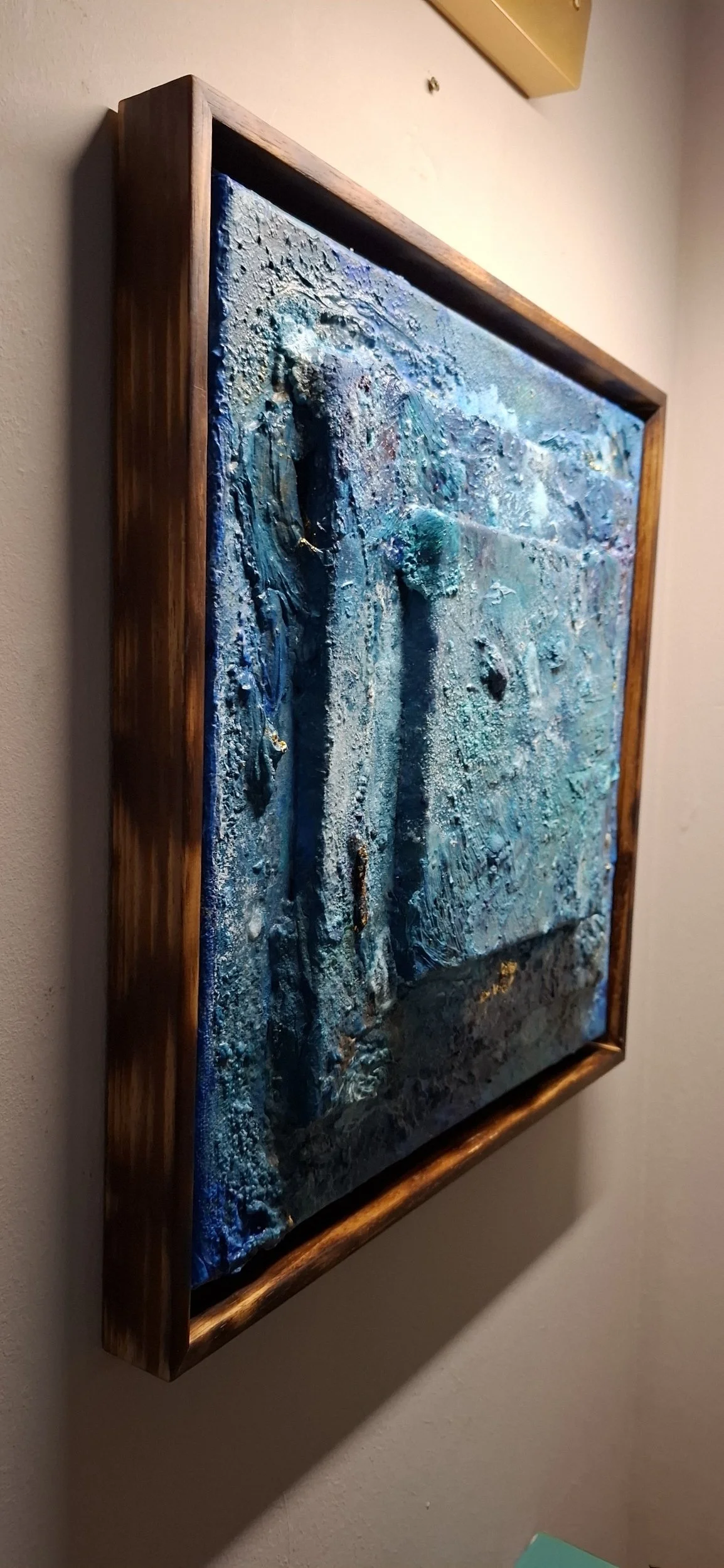 Abstraktes bläuliches Kunstwerk in Holzrahmen an der Wand.