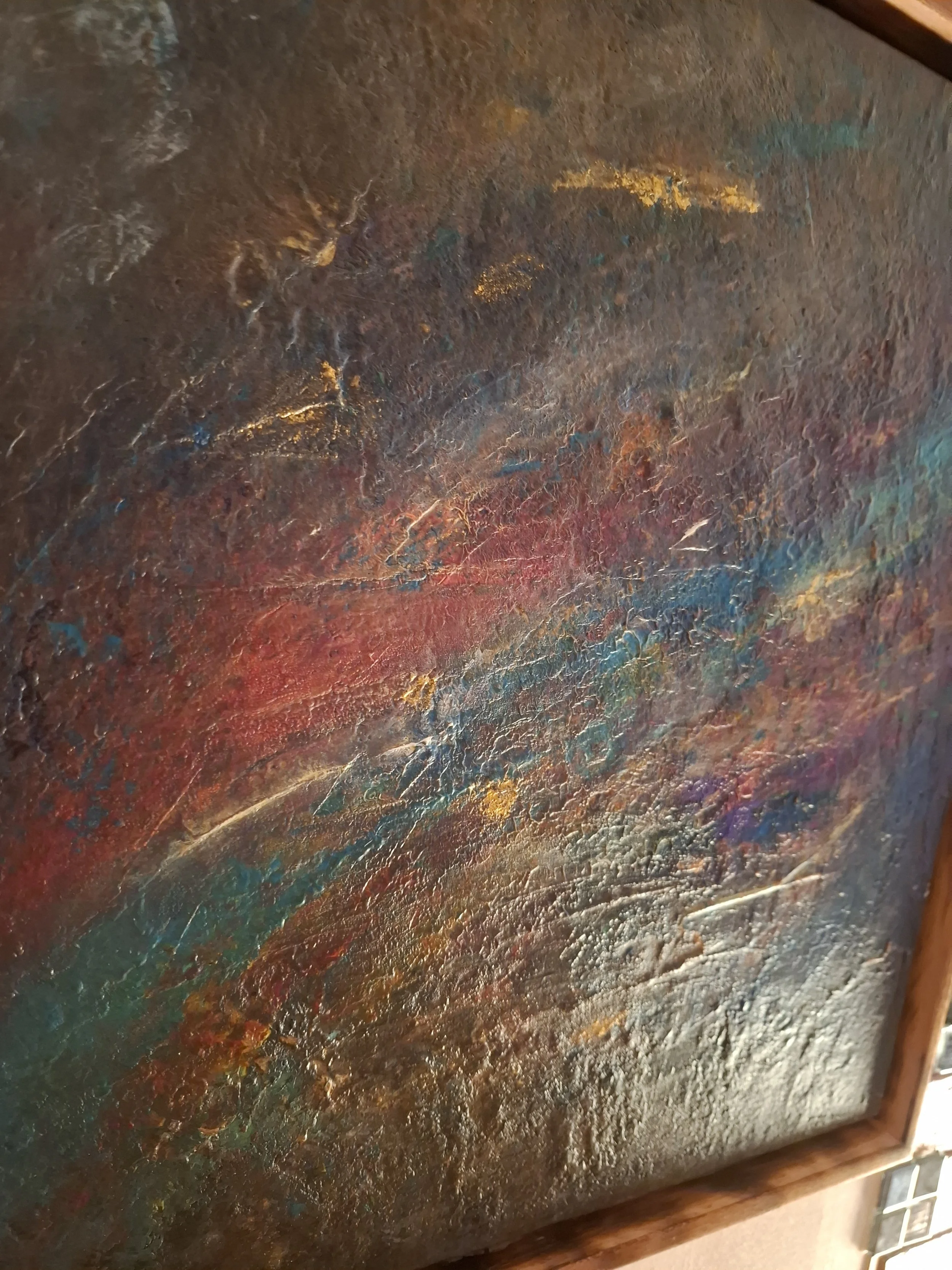 Hier ist eine abstrakte Malerei mit vielen bunten, texturierten Farbflächen, vor allem in Gold, Rot, Blau und Grün, in einem Holzrahmen.