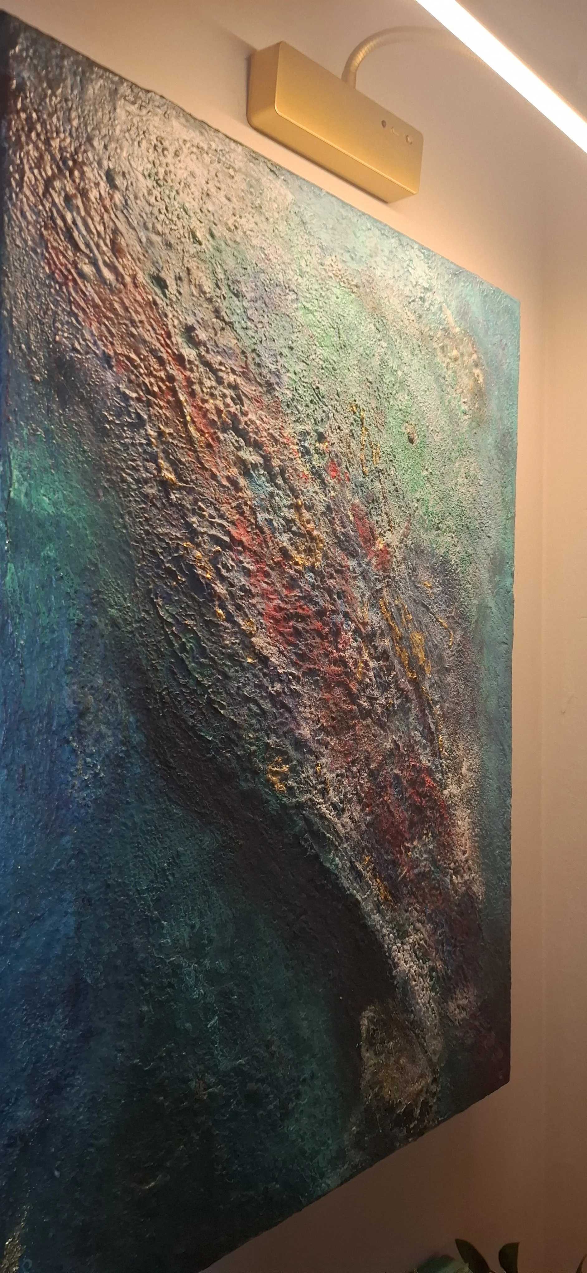Ein abstraktes, farbenfrohes Gemälde mit einer strukturierten Oberfläche und einer Mischung aus Blau, Grün, Rot, Gold und anderen Farben. An der Wand ist eine moderne Wandlampe oder Lichtleiste angebracht.