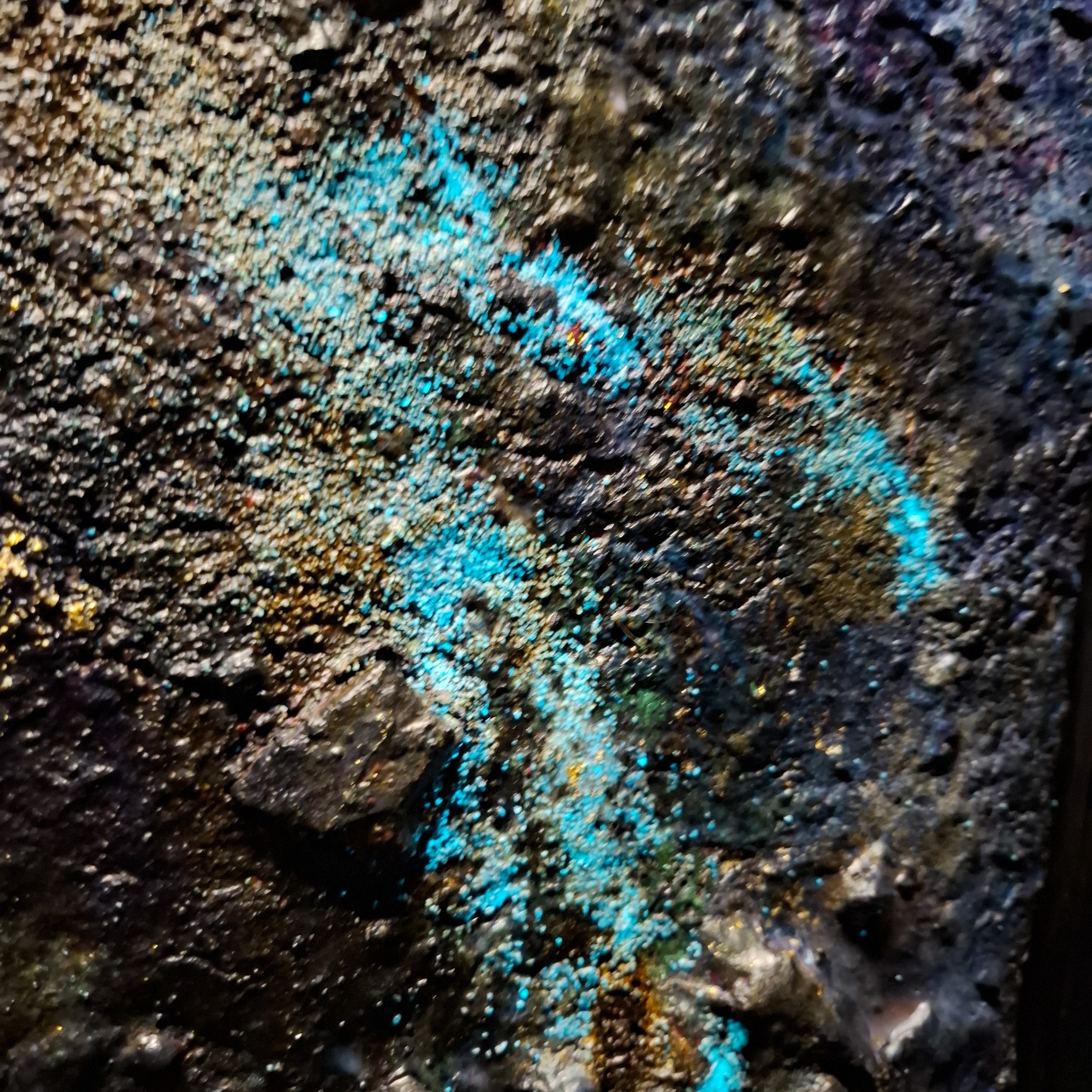 Nahaufnahme von farbigen Sandkörnern mit blauer, goldener, silberner und bunter Reflexionen.