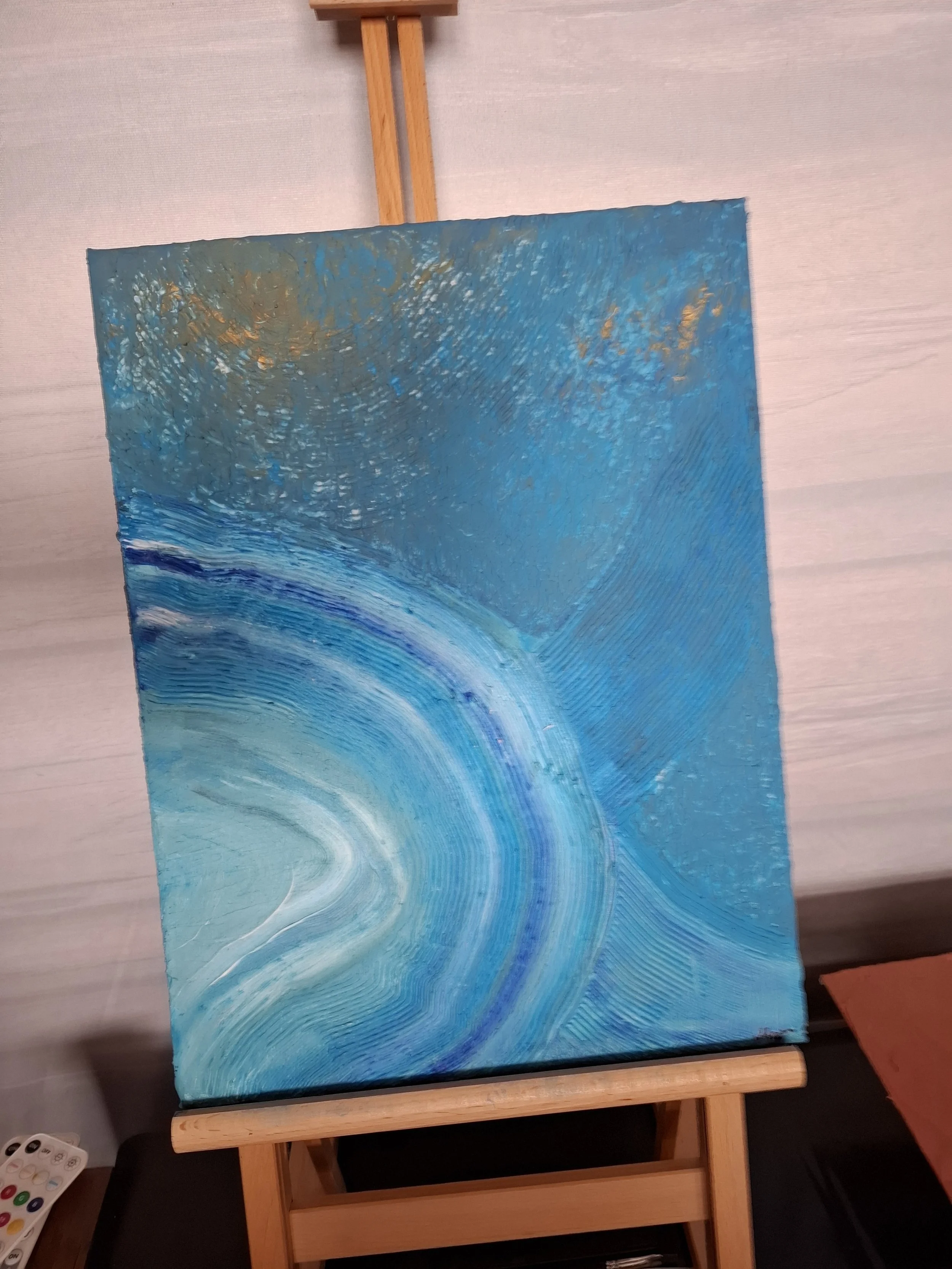 Abstraktes Gemälde mit blauen, weißen und goldenen Farbmustern auf einer Staffelei