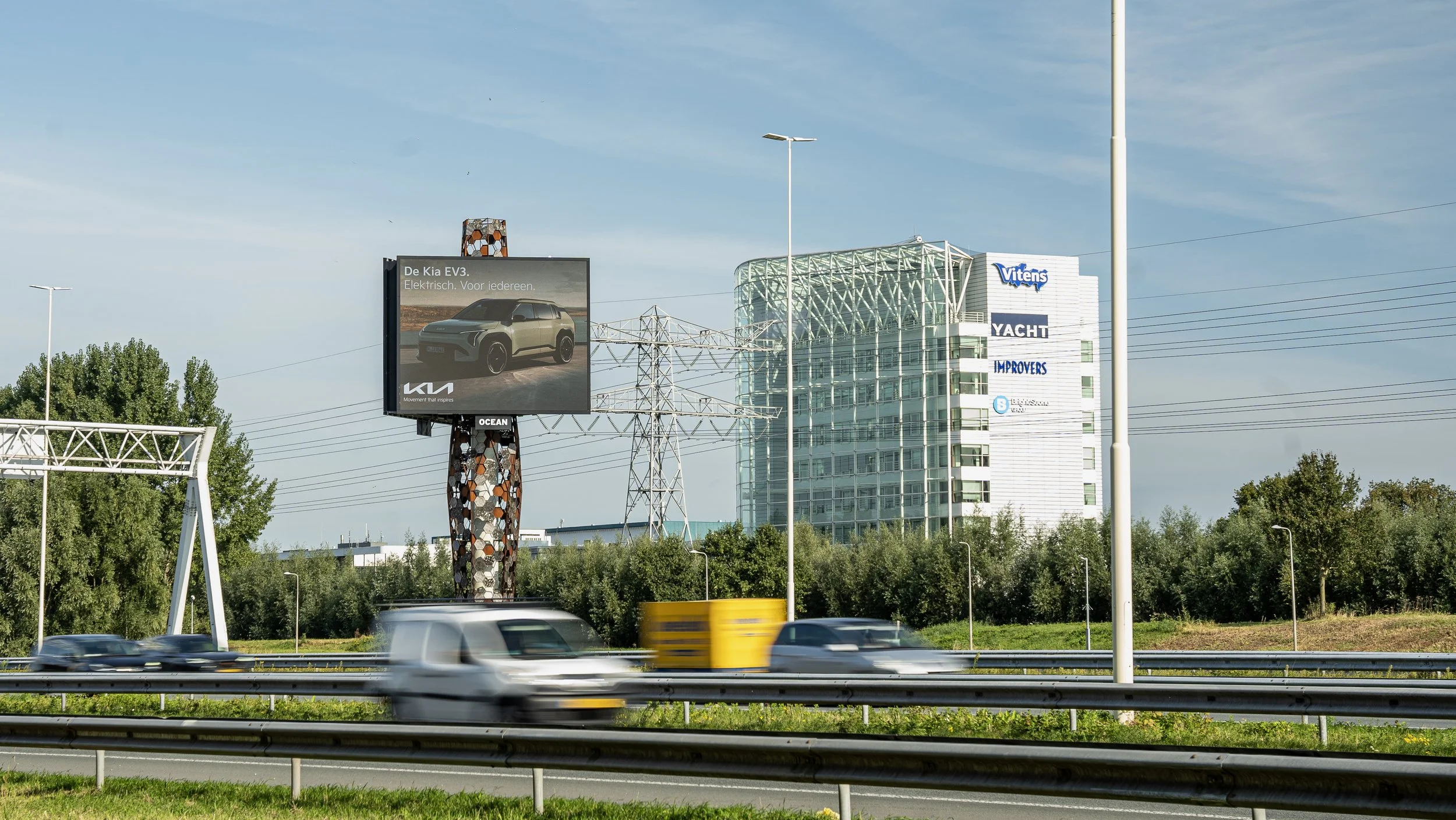 Autos rijden over snelweg met billboard en moderne kantoorgebouwen op achtergrond.