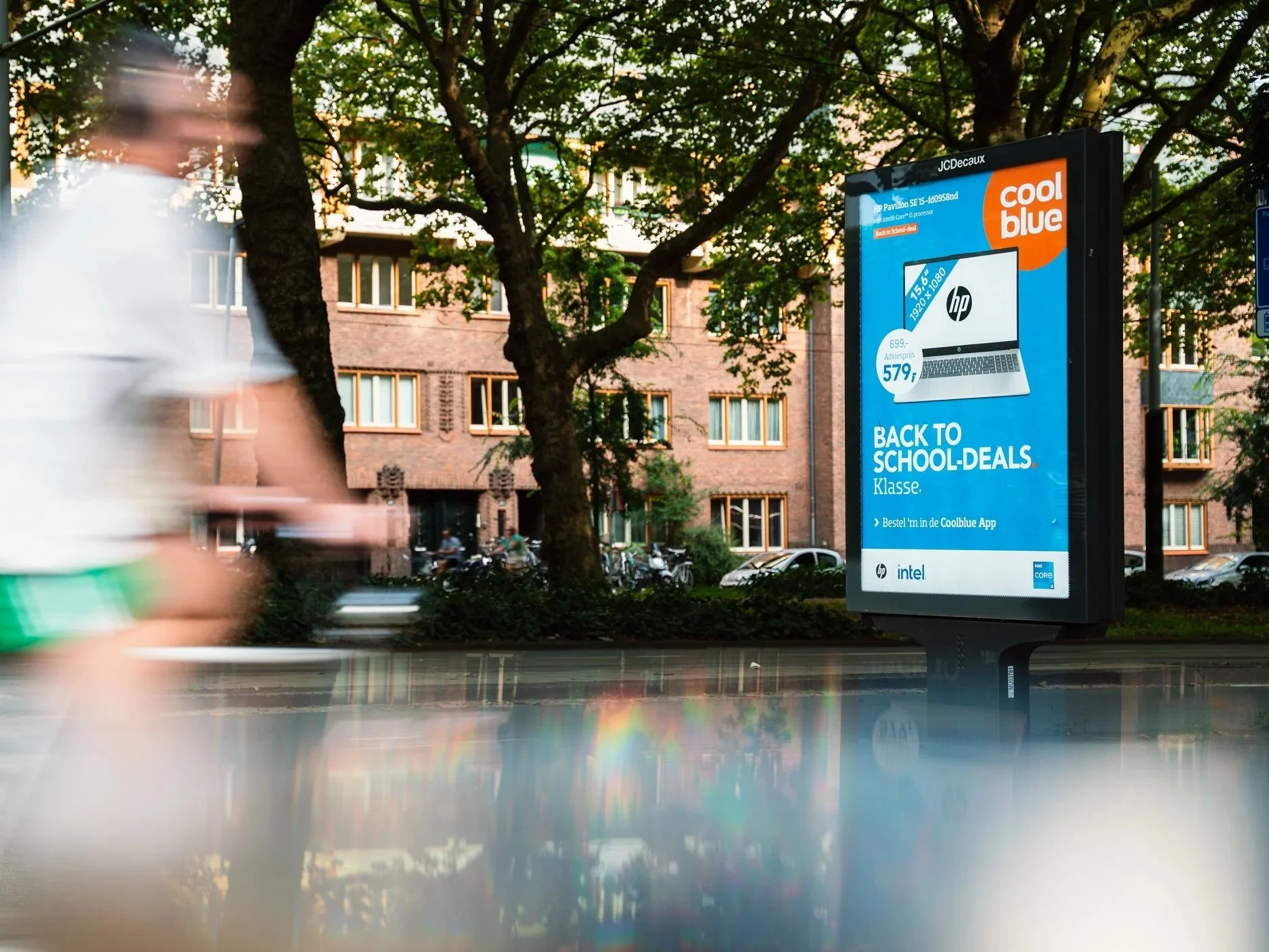 Digitale reclamezuil op straat met campagne voor back-to-school deals, met een afbeelding van een HP laptop en tekst in het Nederlands.