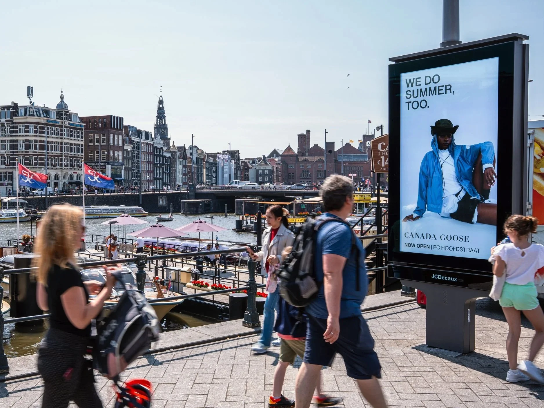 Gezicht op een stad aan een grachten met mensen die langs de waterkant lopen en een advertentiebord voor Canada Goose.
