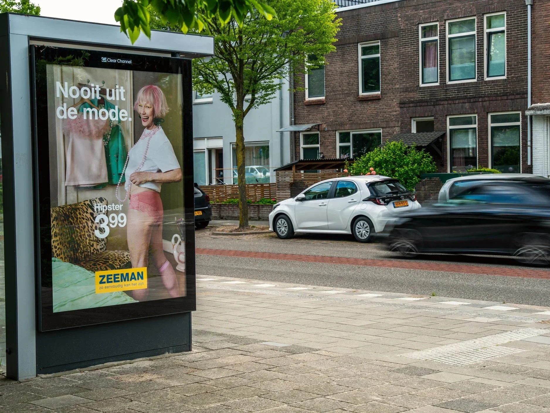 Een bushokje met een reclameposter van Zeeman, waarop een vrouw met roze haar en outfit uit de jaren 80 te zien is.