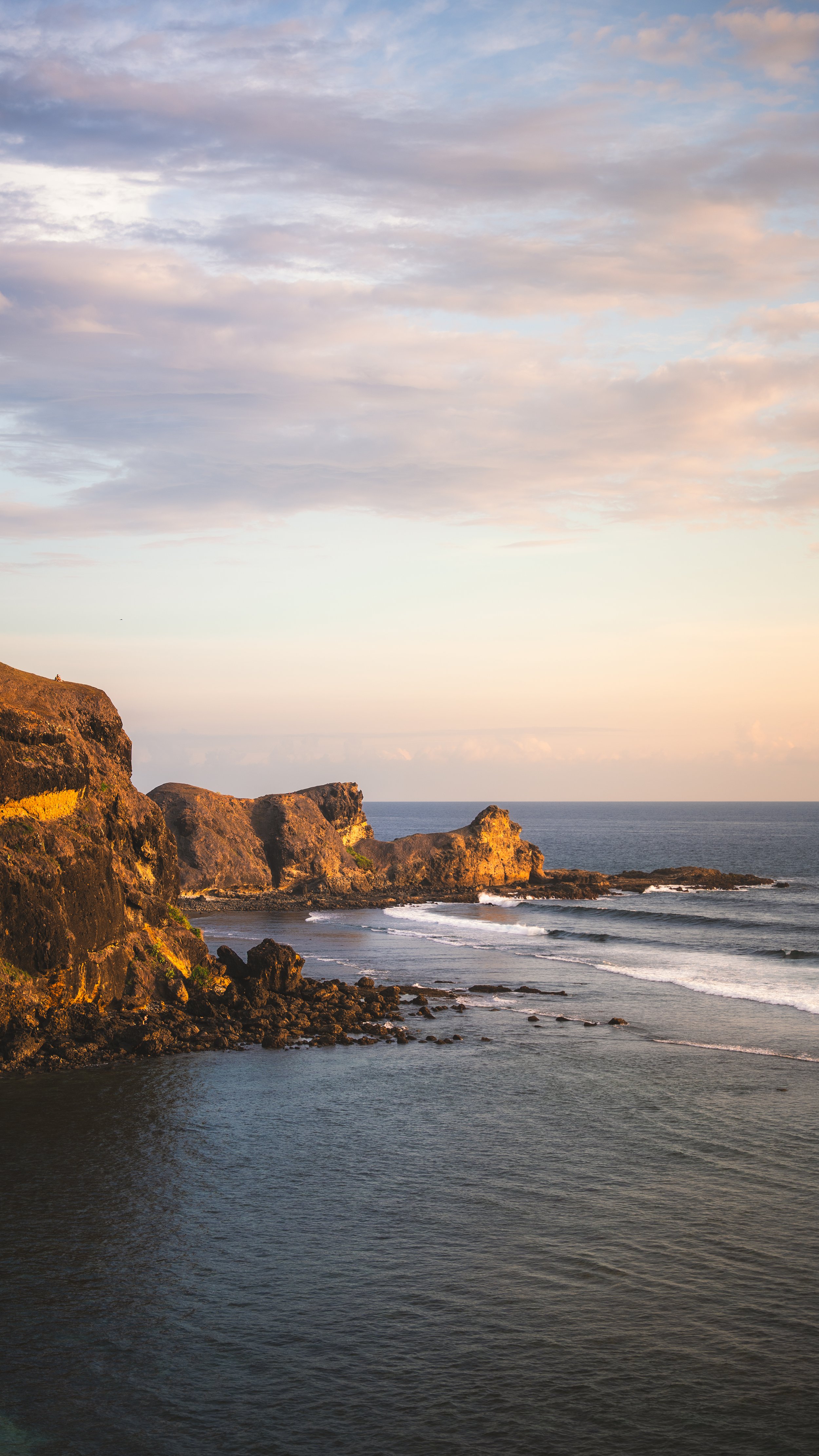 Een kustlandschap met rotsformaties, de oceaan en een sky met wolken tijdens zonsondergang.