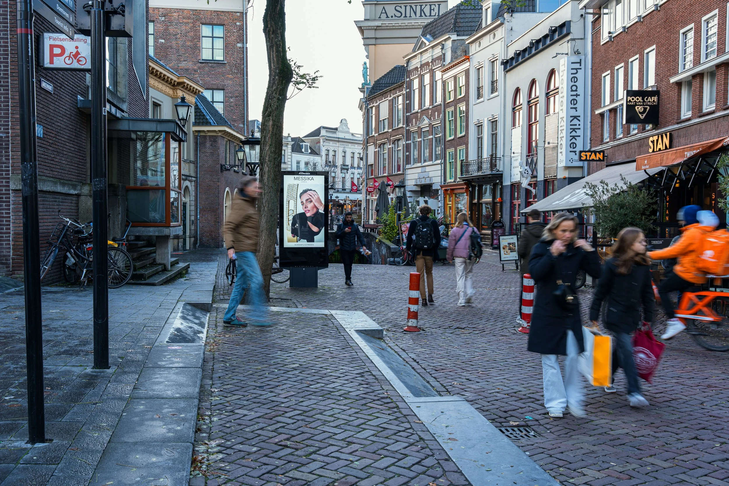 Straatbeeld in Utrecht met voetgangers, fietsers en gezellige winkels, onder een bewolkte hemel.
