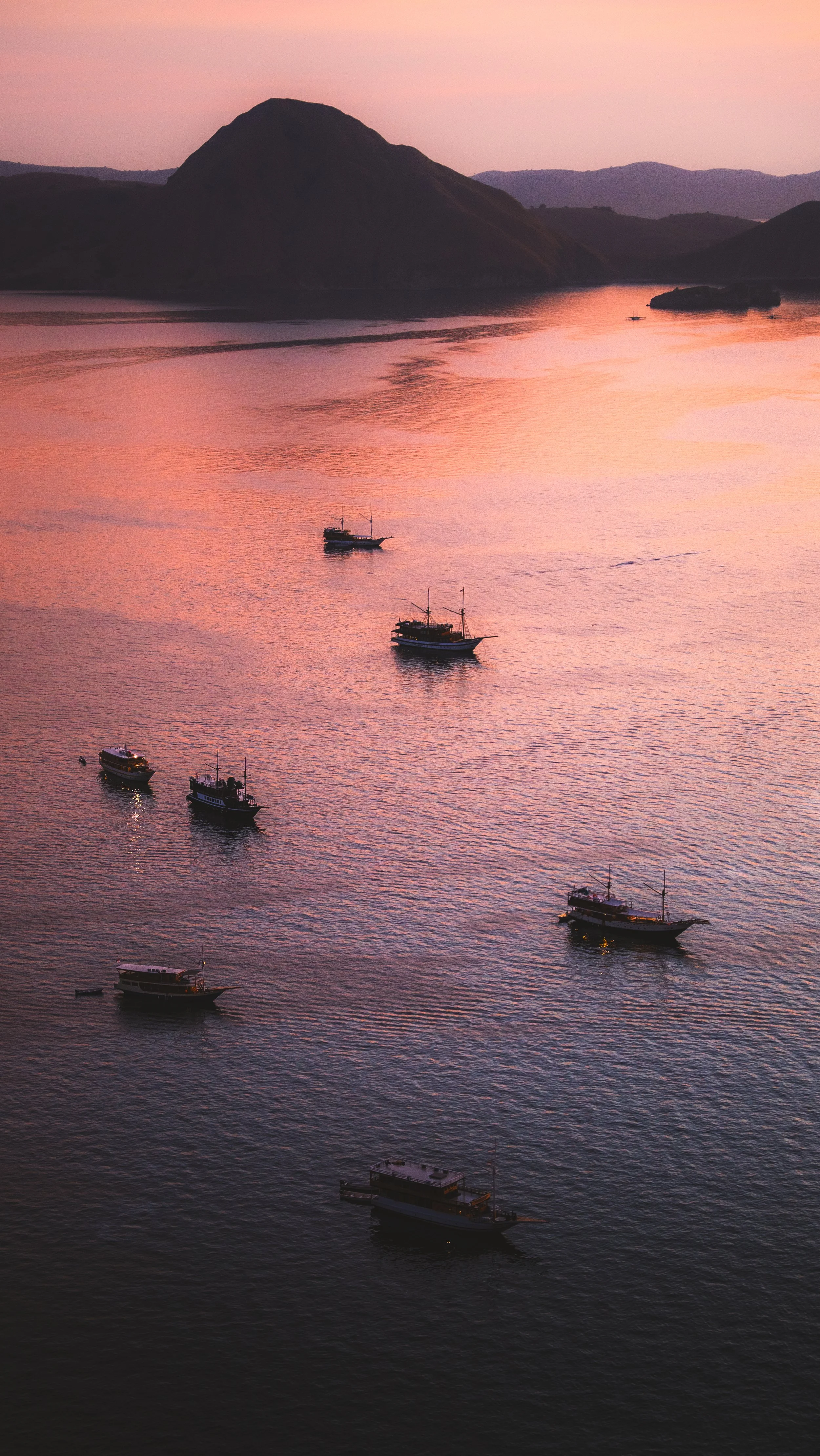 Zeven schepen op kalmend water bij zonsondergang met heuvels op achtergrond