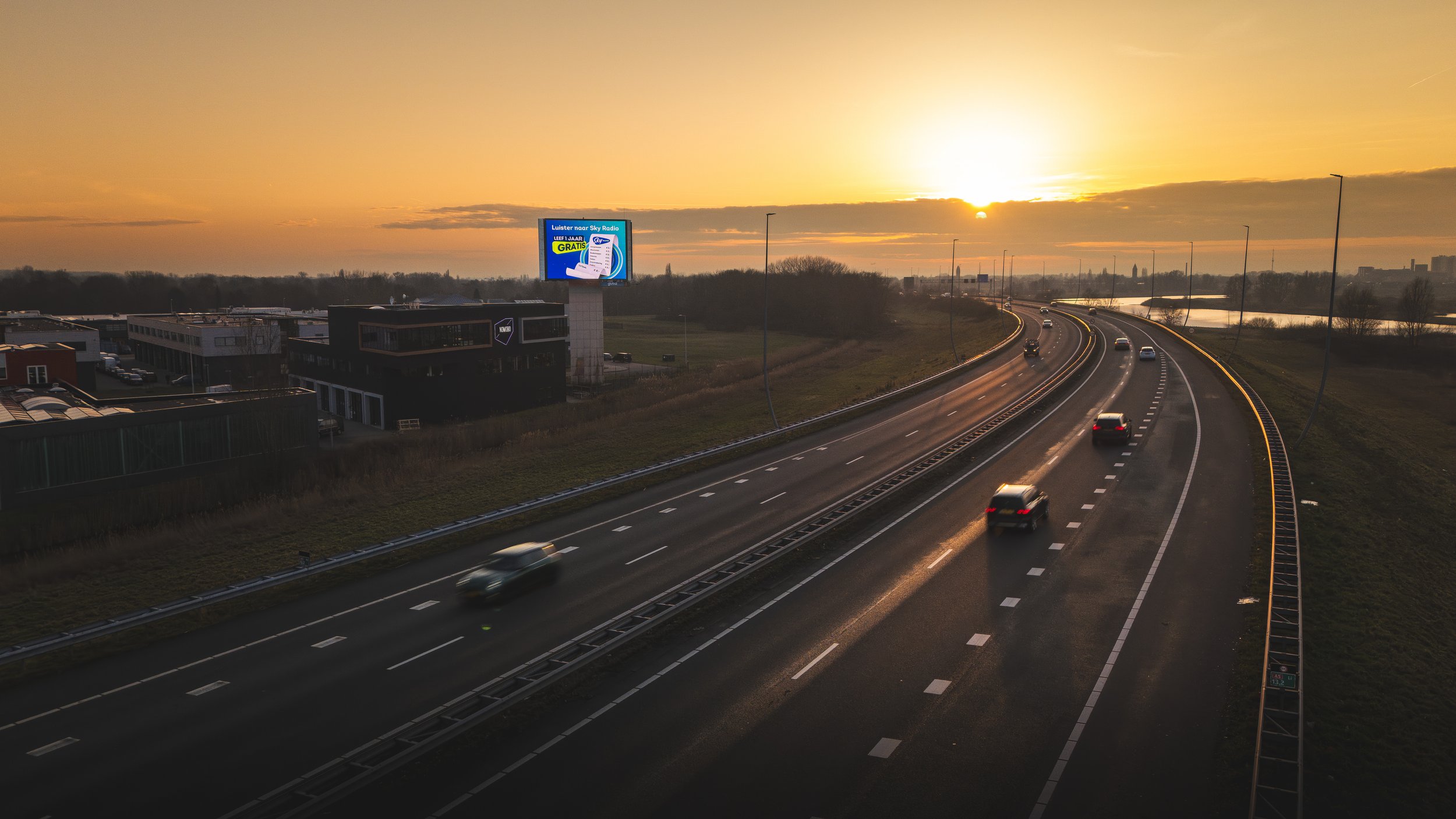 Een snelweg bij zonsondergang met enkele rijdende auto's en een billboard op de achtergrond.