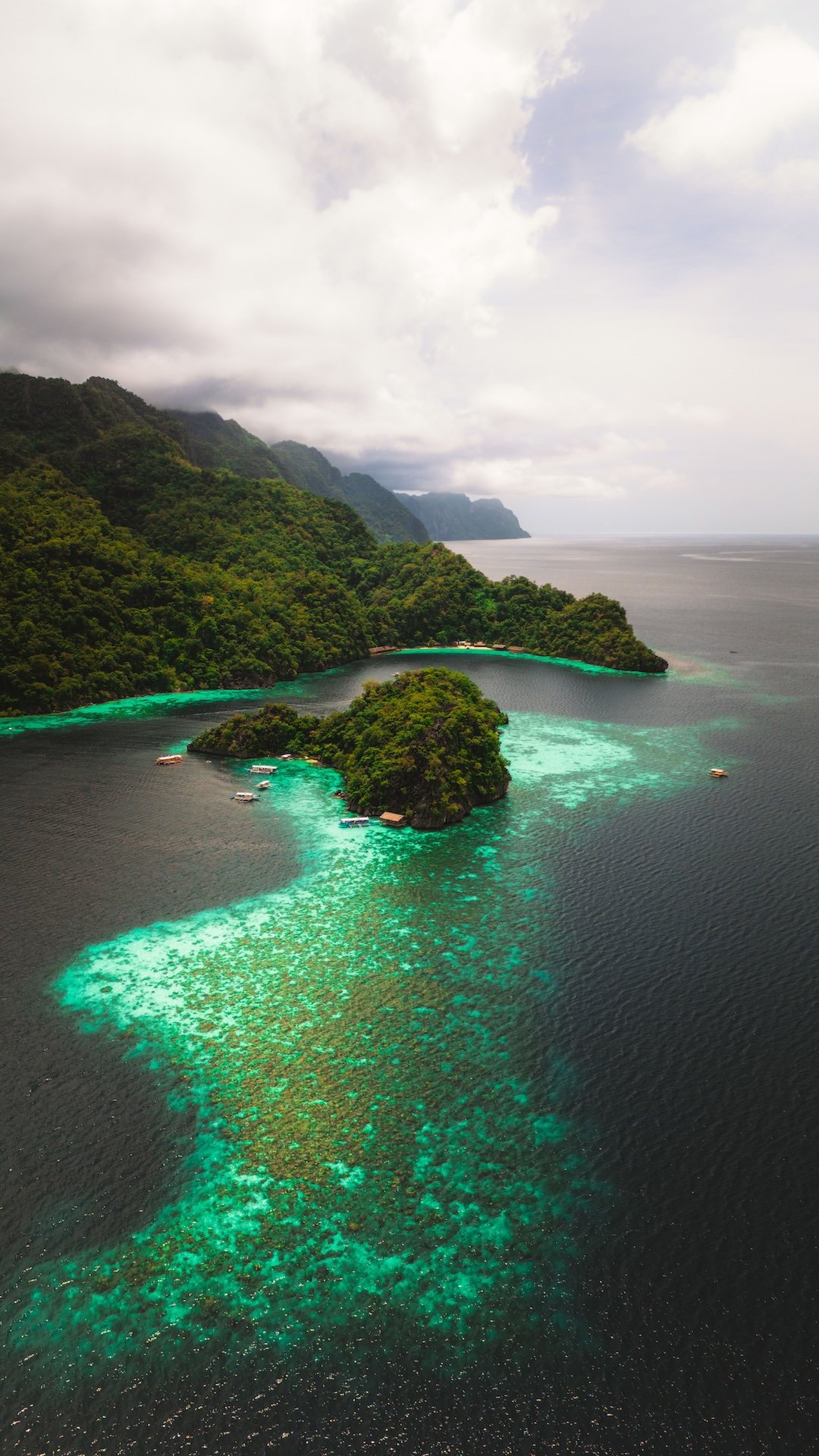 Landschap met groene eilanden en turquoise water, omgeven door een bergketen onder een bewolkte lucht.