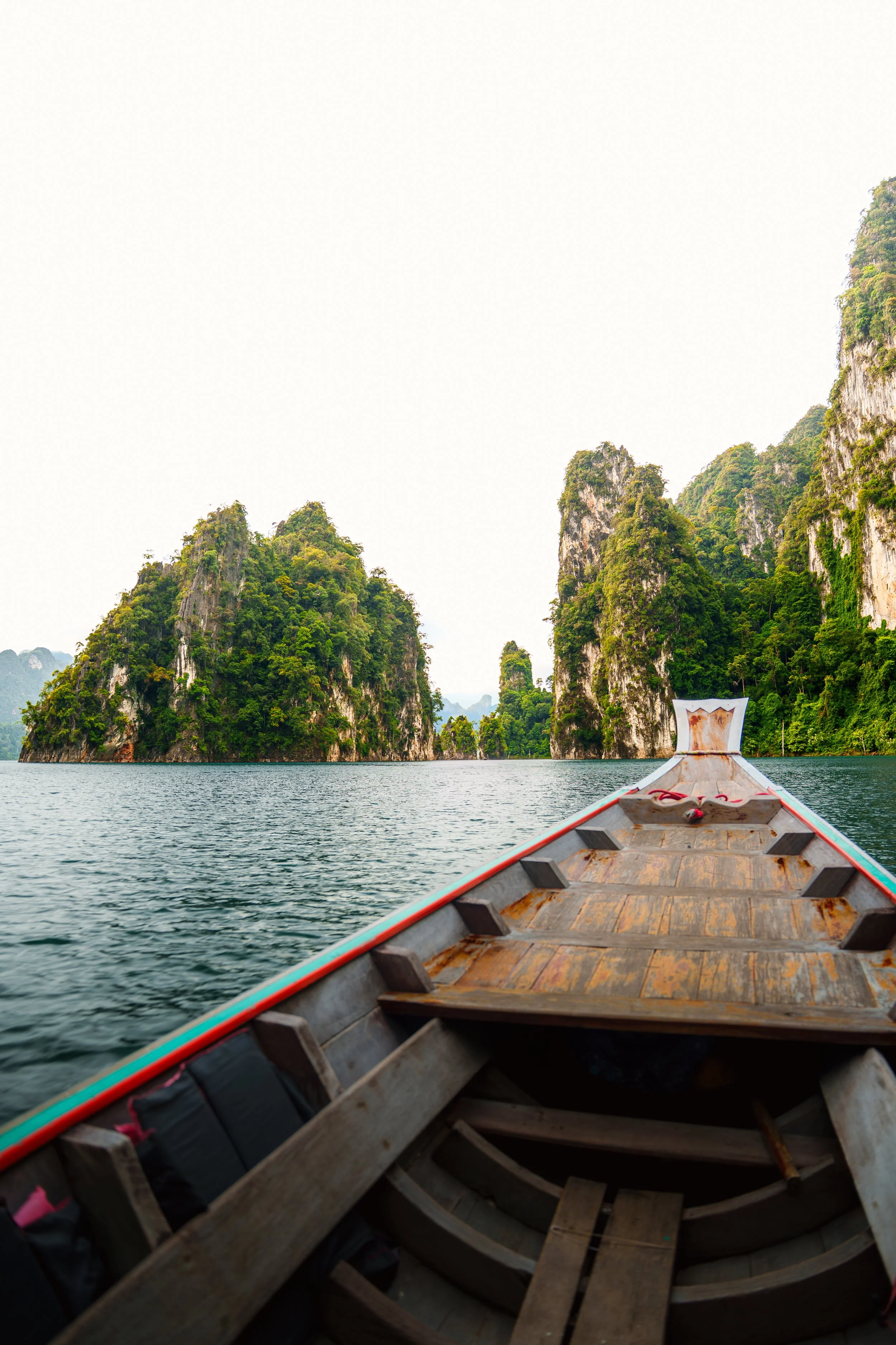 Een boot op een rustig meer met groene, kalkstenen eilanden op de achtergrond onder een witte, bewolkte lucht.