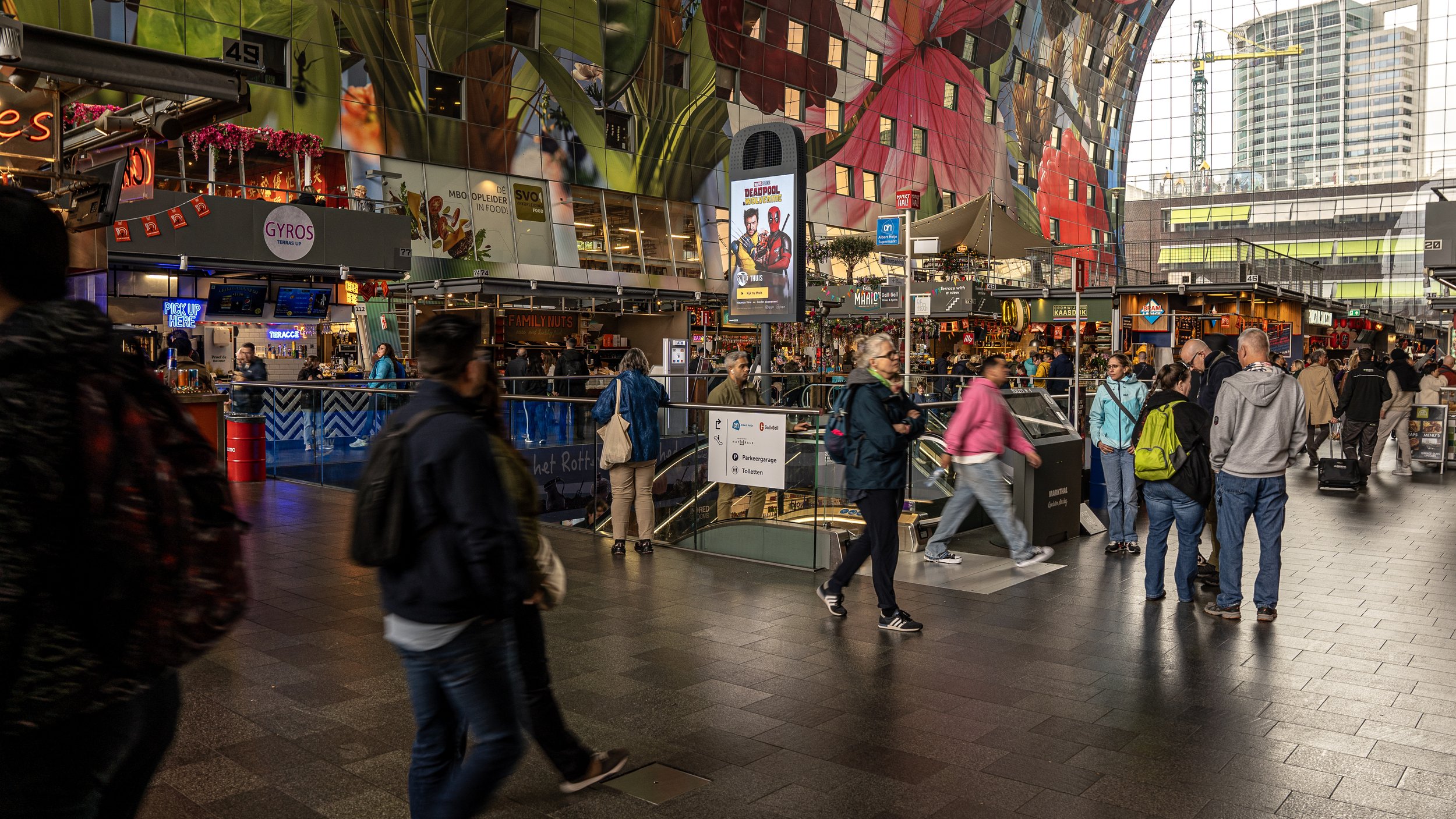 Binnenstad met mensen die naar beneden gaan en wachten, kleurrijk modern gebouw met grote schermen en verschillende winkels.