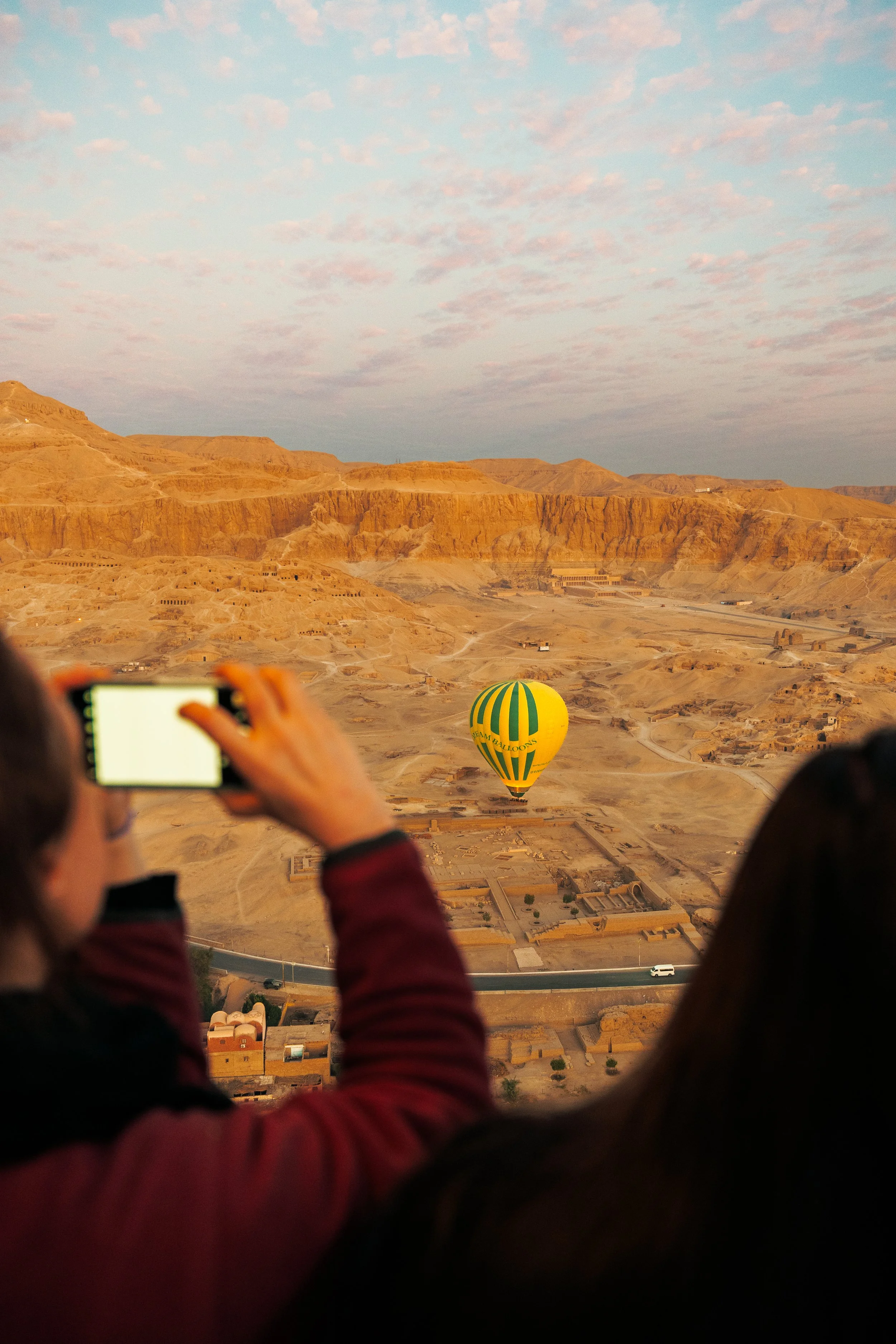 Twee mensen kijken naar een gele en groene fietsballon in een woestijnachtig landschap met bergen op de achtergrond.