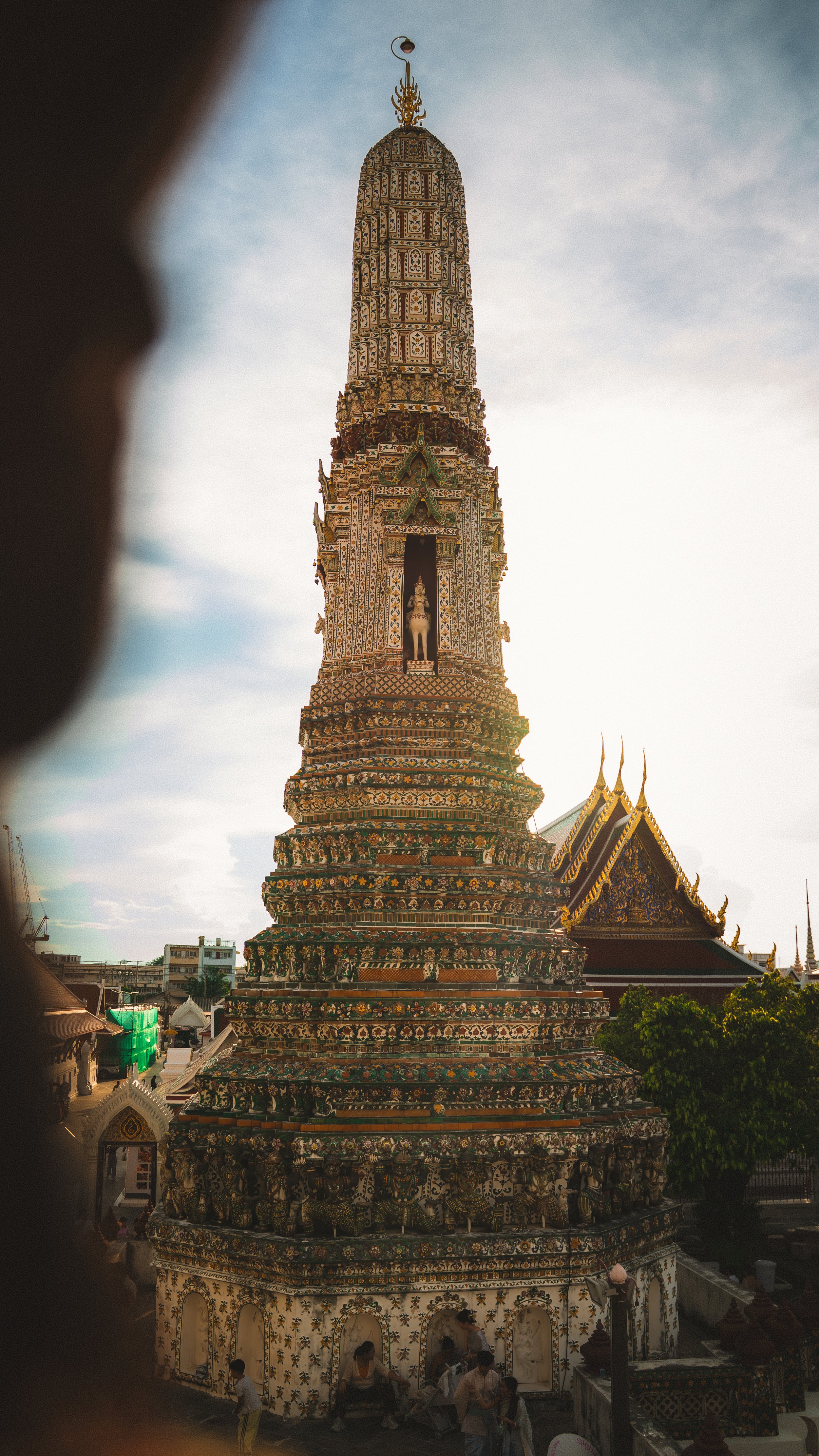 Een grote, versierde tempelspits in Thailand, met mensen eromheen die de tempel bekijken.