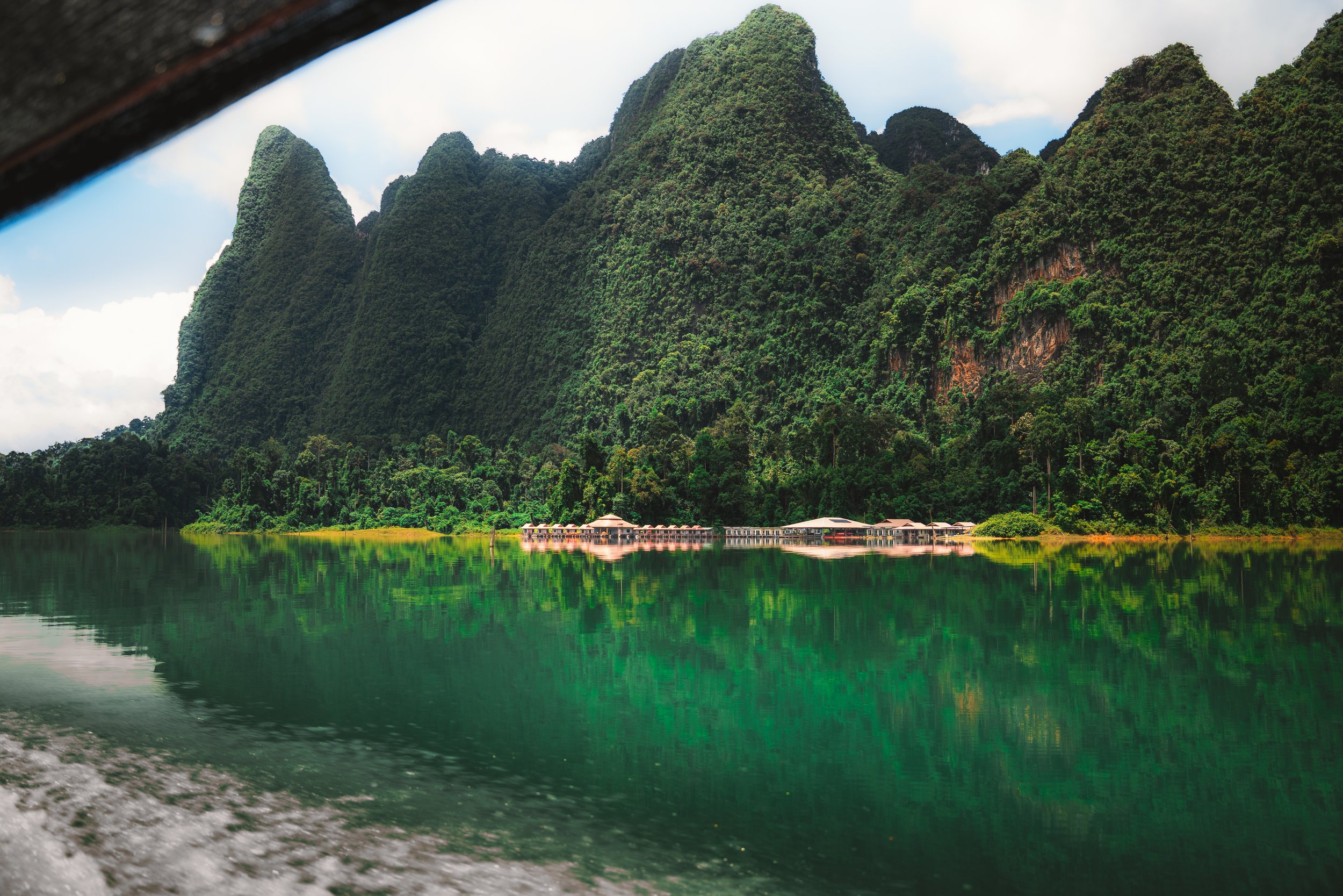 Mooie groene bergen met een nederzetting langs de waterkant, gezien vanaf een boot, met reflectie in het water.