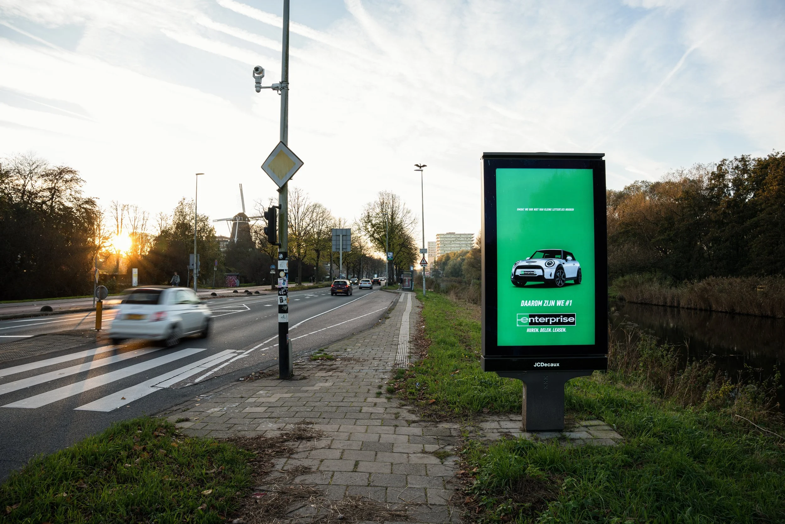 Elektronische reclamebord langs een weg met groen achtergrond en een witte auto, met tekst in het Nederlands.