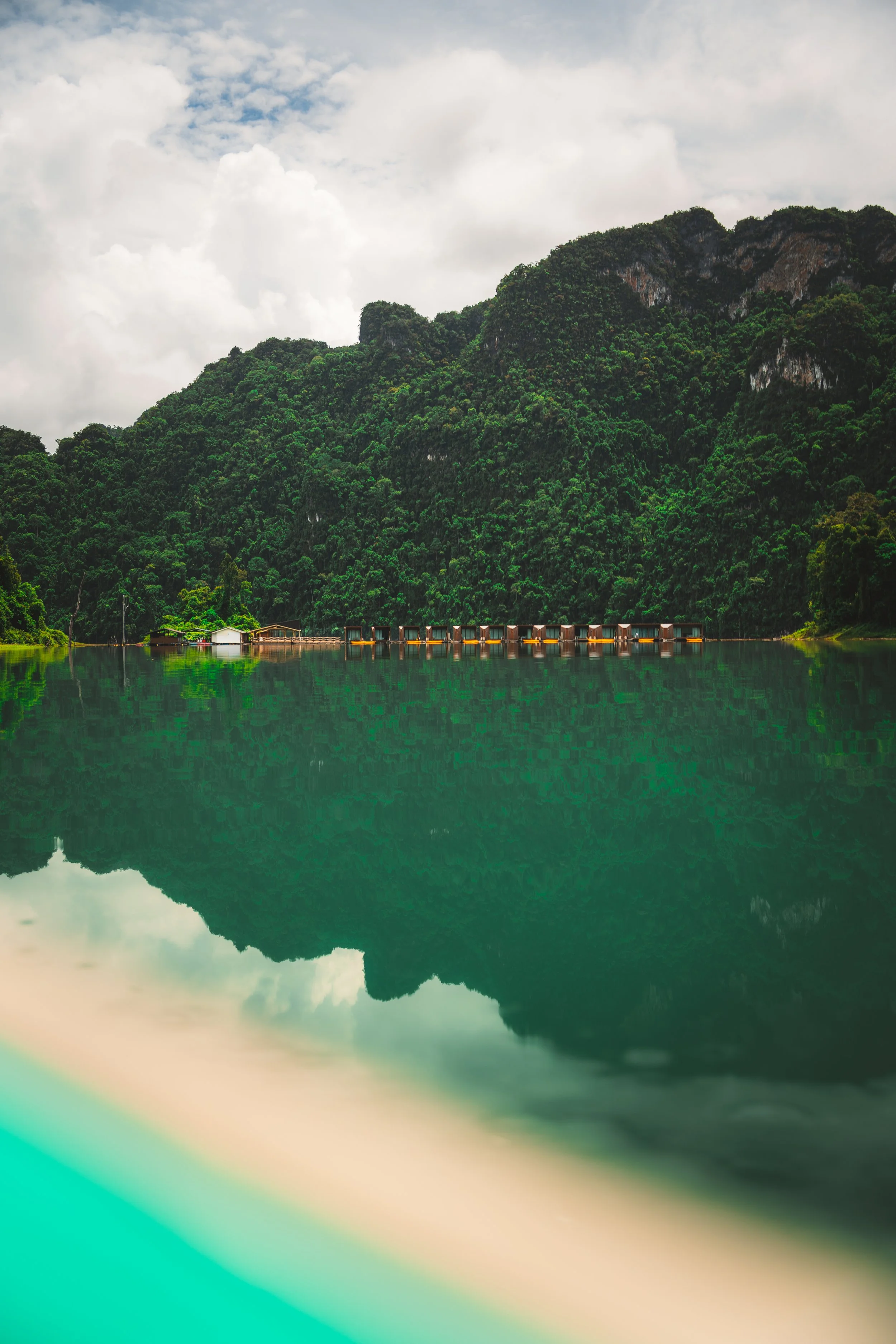 Natuurscène met groene bergen en een wateroppervlak dat de berg en de wolken weerspiegelt.