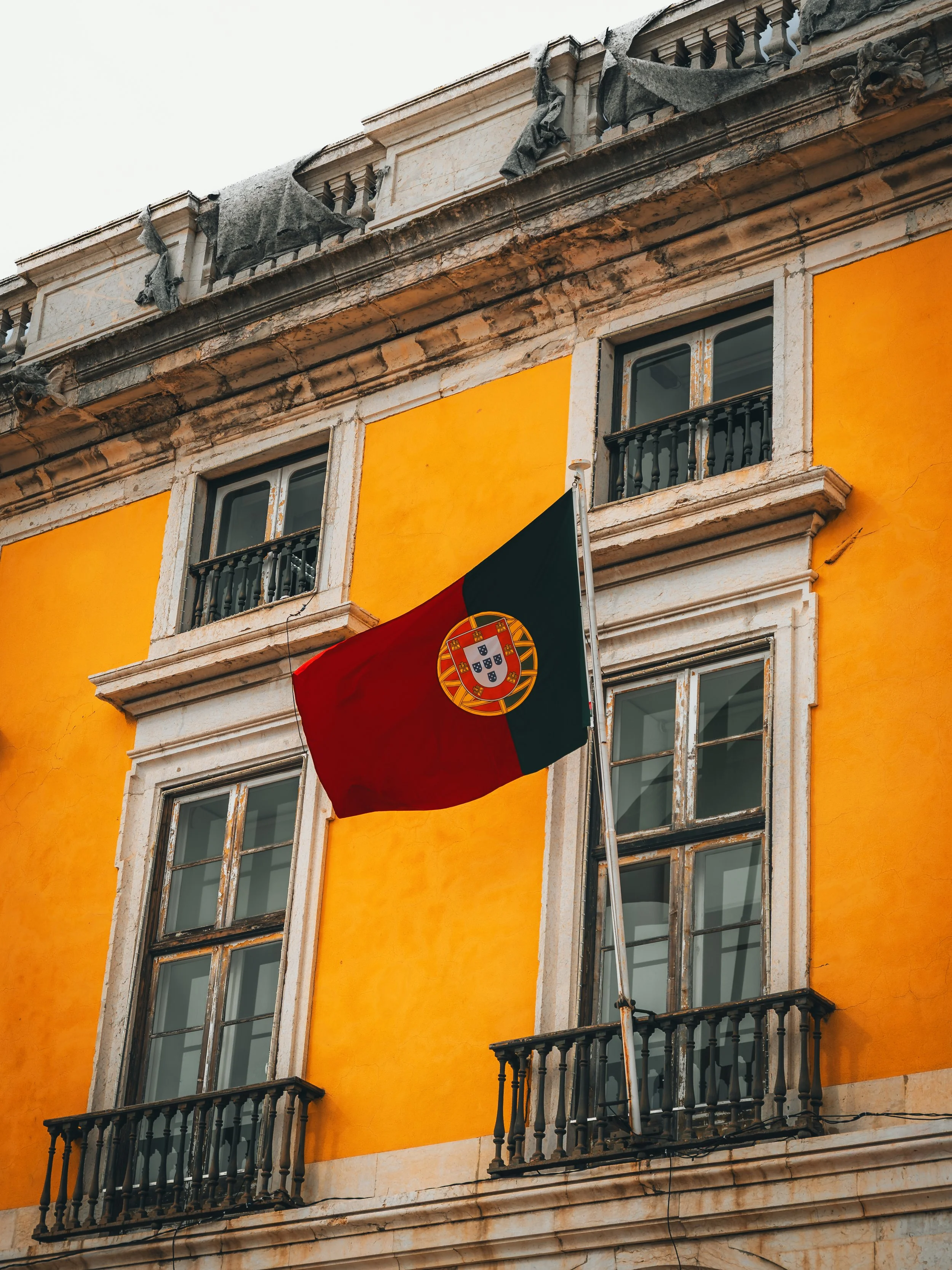 Portugese vlag hangt voor een geel gebouw met meerdere ramen en balkonnetjes.