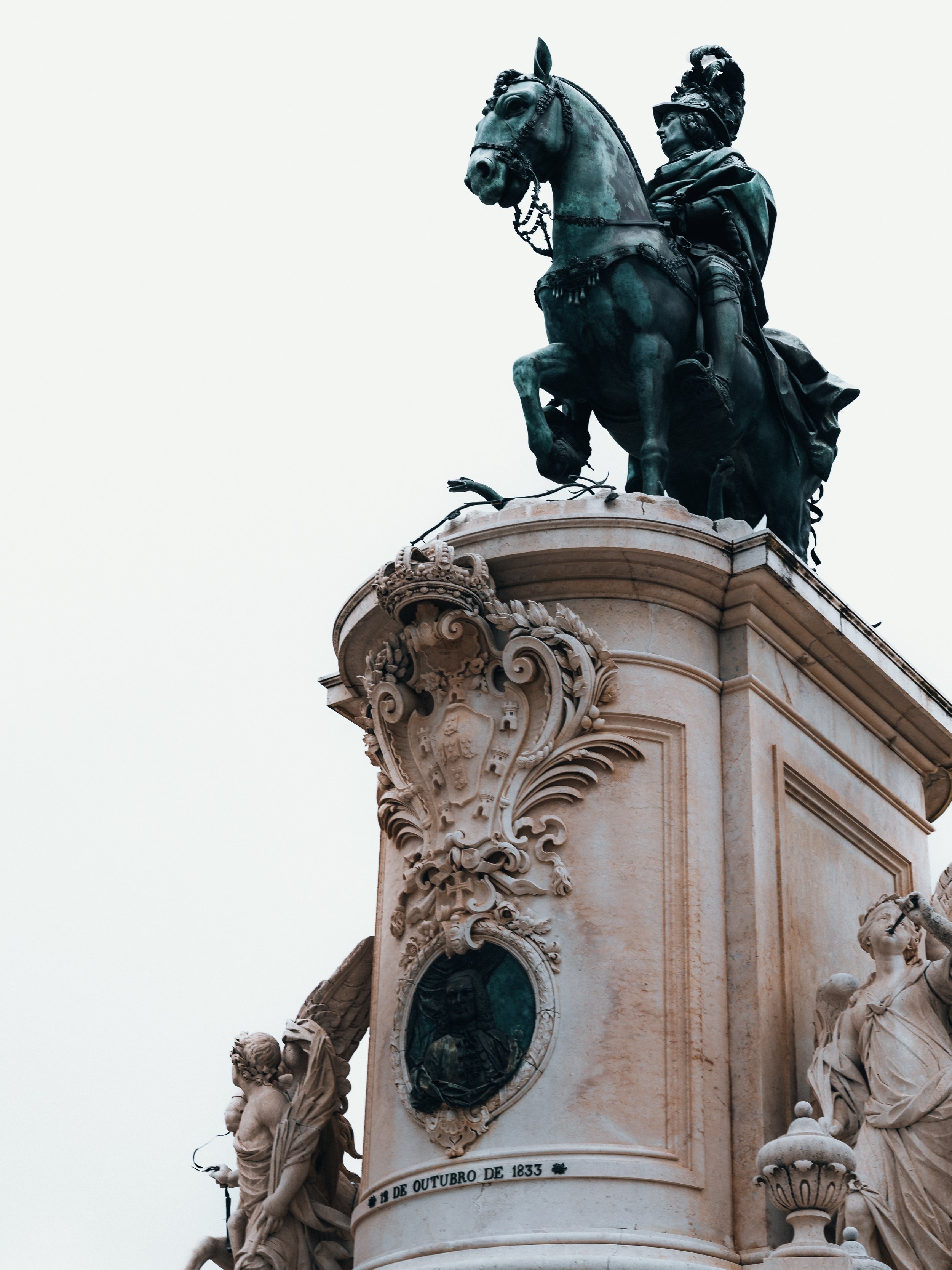 Een standbeeld van een ruiter op een paard op een monument met gedetailleerde ornamenten en reliëfs.