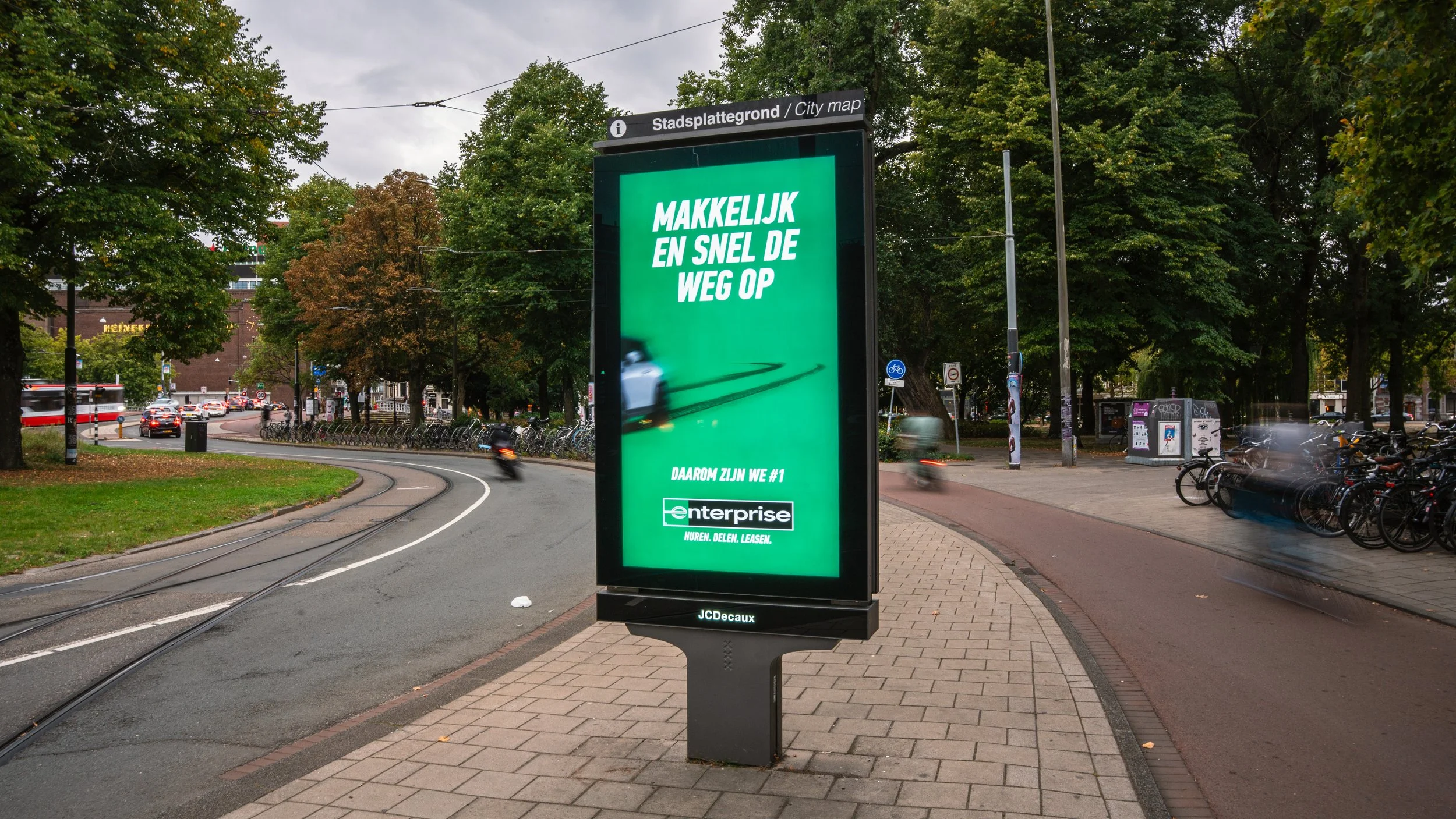Elektronische bushalte midden op straat met een groene reclamebanner die zegt: 'Makkelijk en snel de weg op' en onderaan het logo van enterprise.