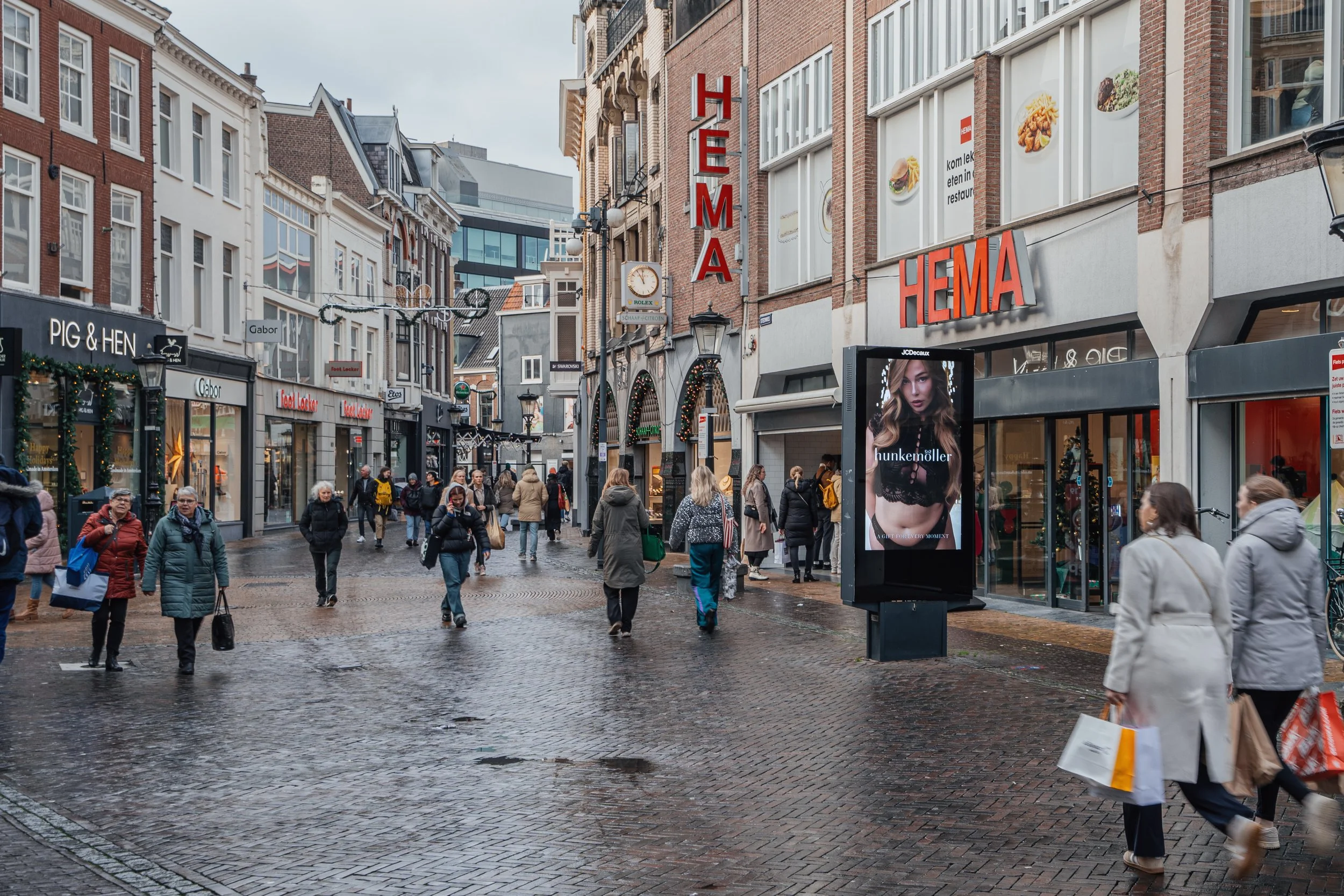 Winkelstraat met diverse winkels en mensen die winkelen, op een bewolkte dag.