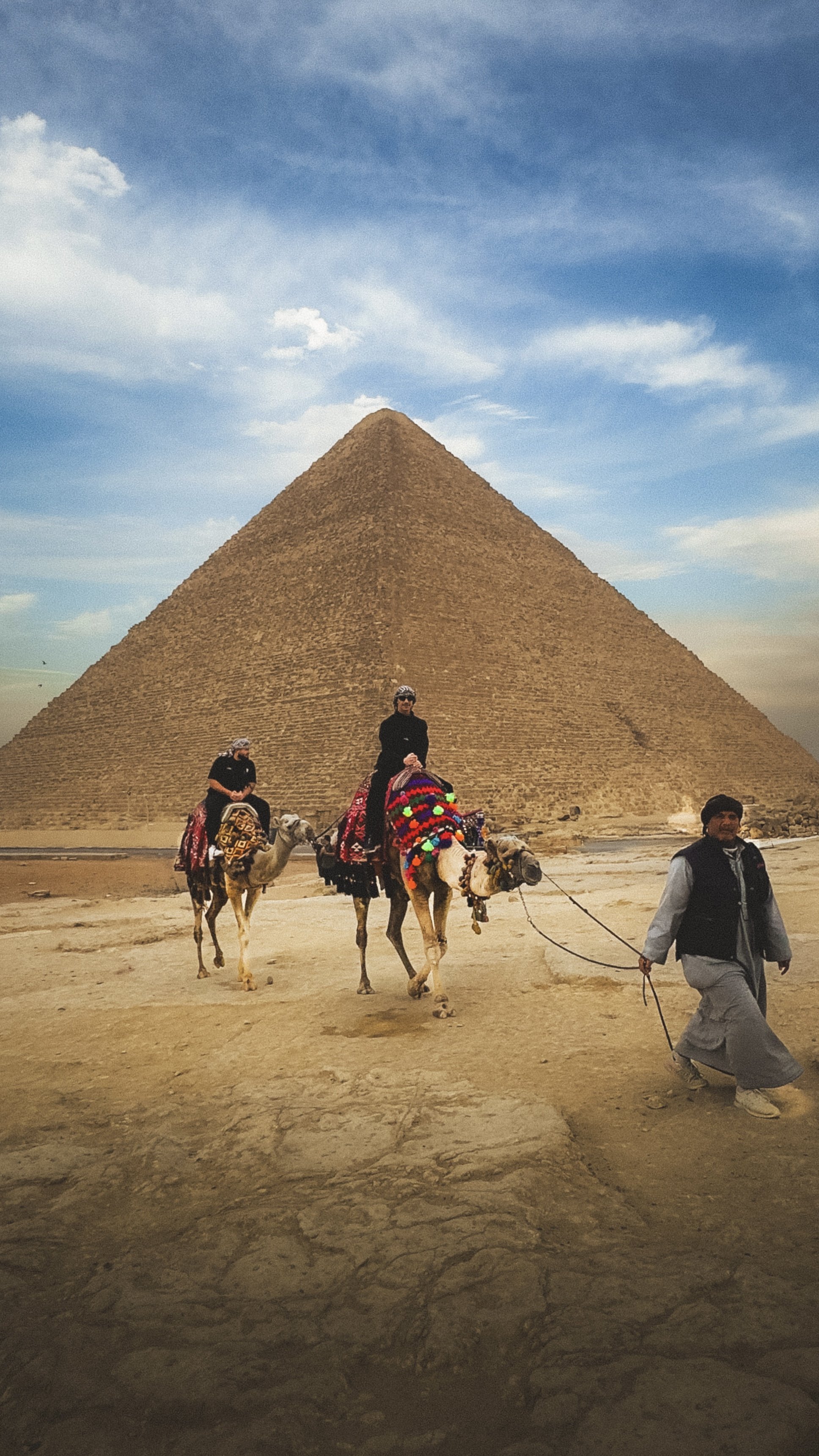 Twee mensen rijden op kamelen voor de piramide van Gizeh in Egypte, met een man die de kamelen leidt.
