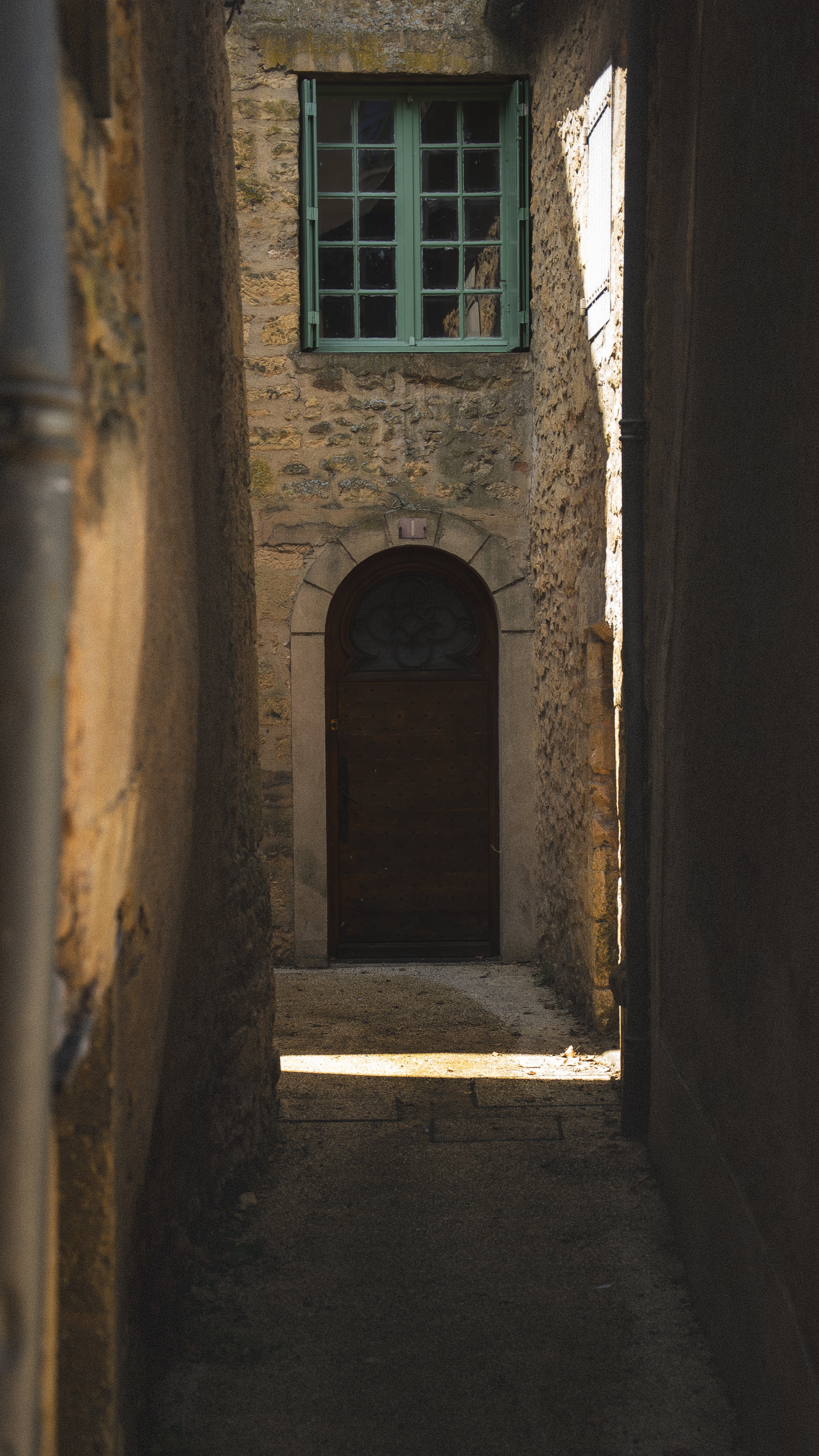 Smalle straat tussen oude stenen gebouwen, met een houten deur en een groene raam op de achtergrond.