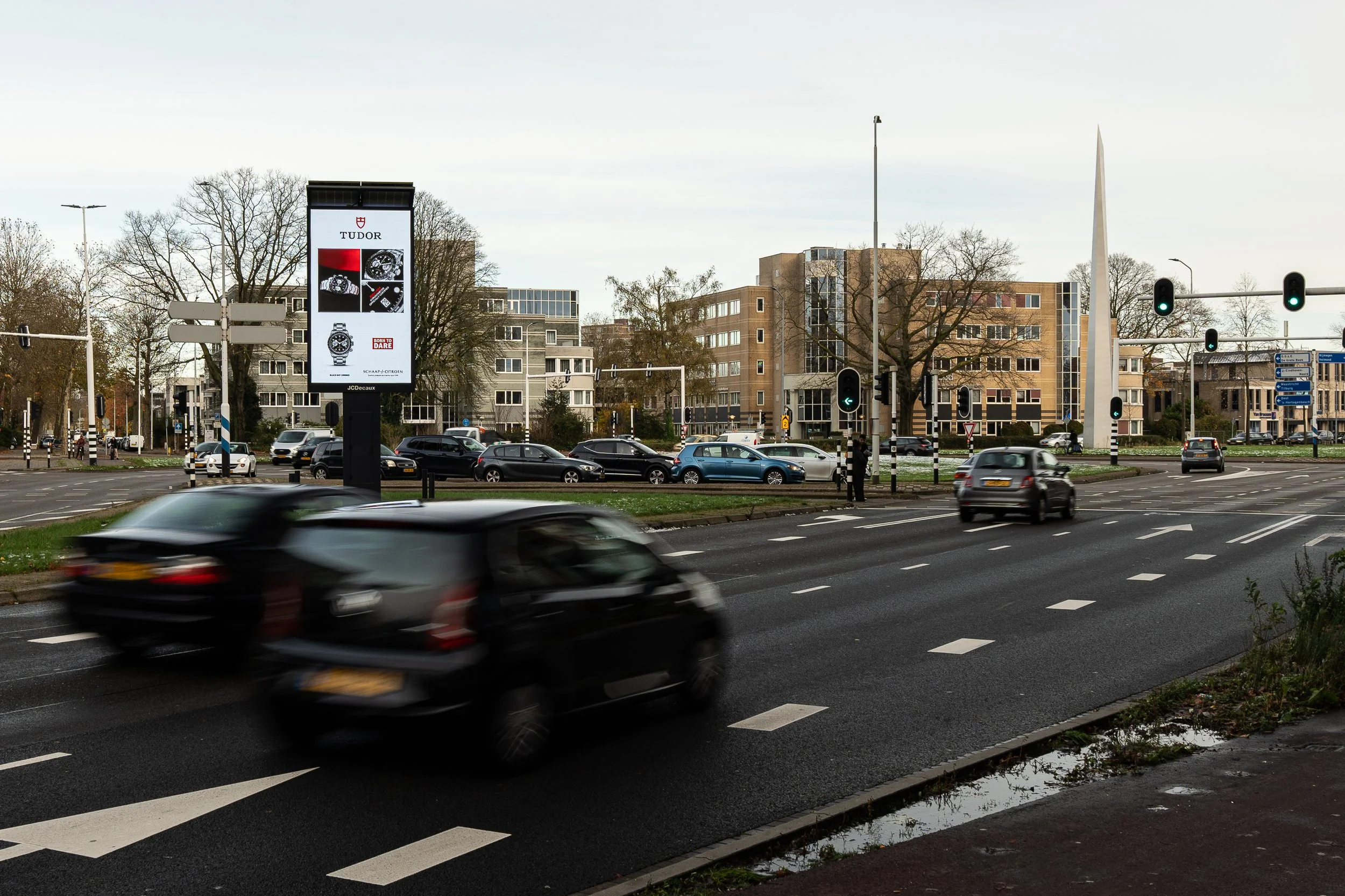 Straat met autoverkeer, verkeerslichten, billboards, bomen en gebouwen in de achtergrond.